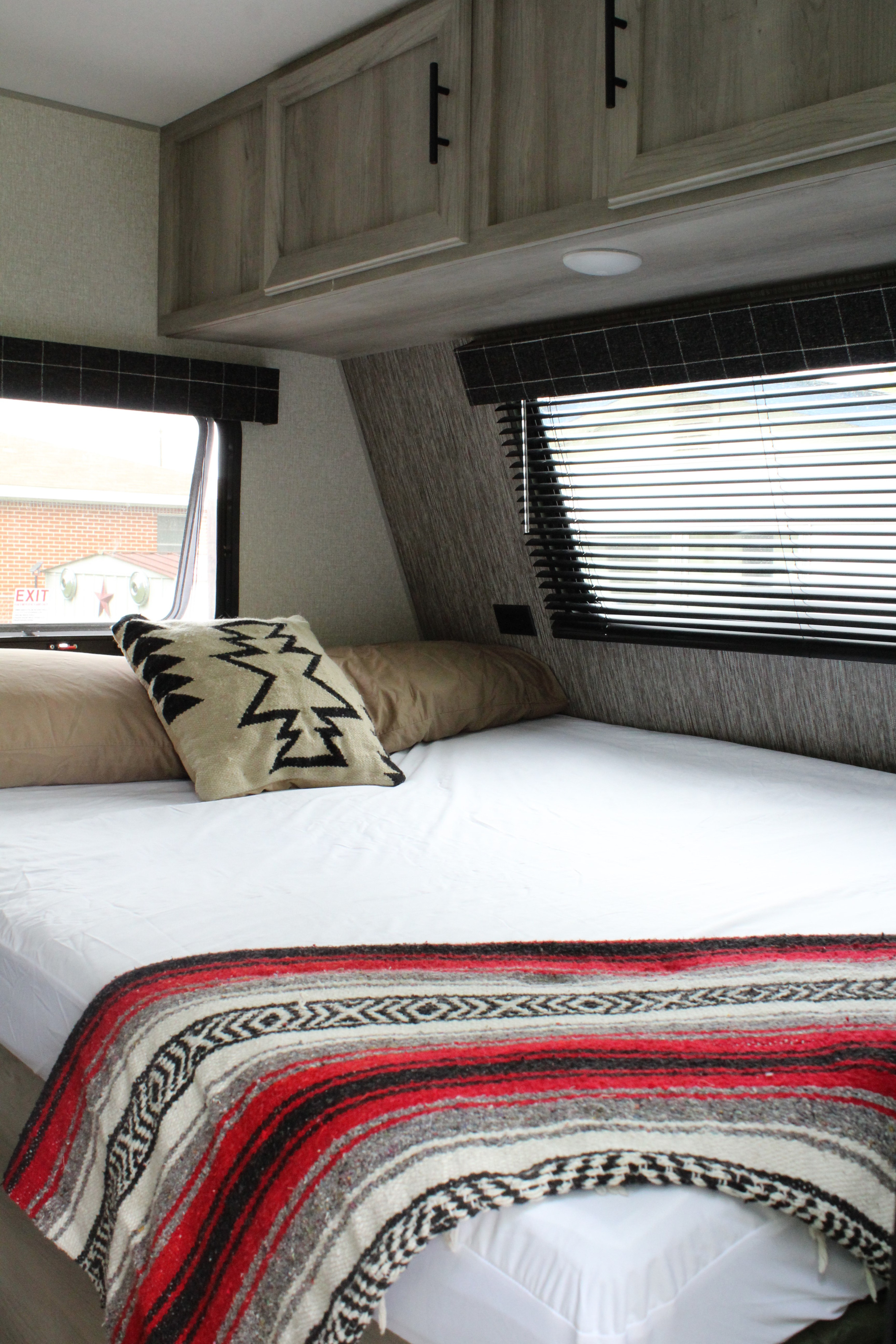 RV rental bedroom interior, showcasing a comfy bed with a patterned blanket, overhead cabinets, and windows.. KZ Sportsmen Classic 191BHK 2022