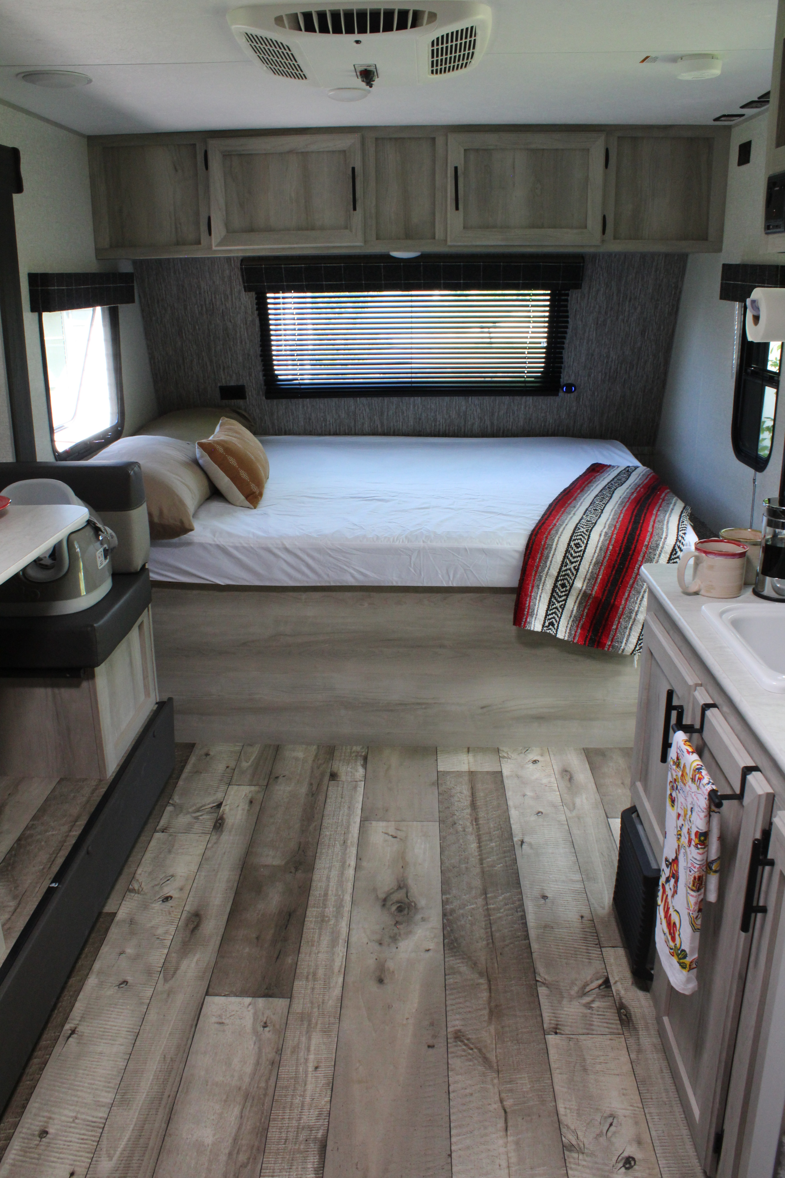 Cozy RV rental interior featuring a bed, overhead cabinets, and wood-look flooring, with a glimpse of the kitchen.. KZ Sportsmen Classic 191BHK 2022