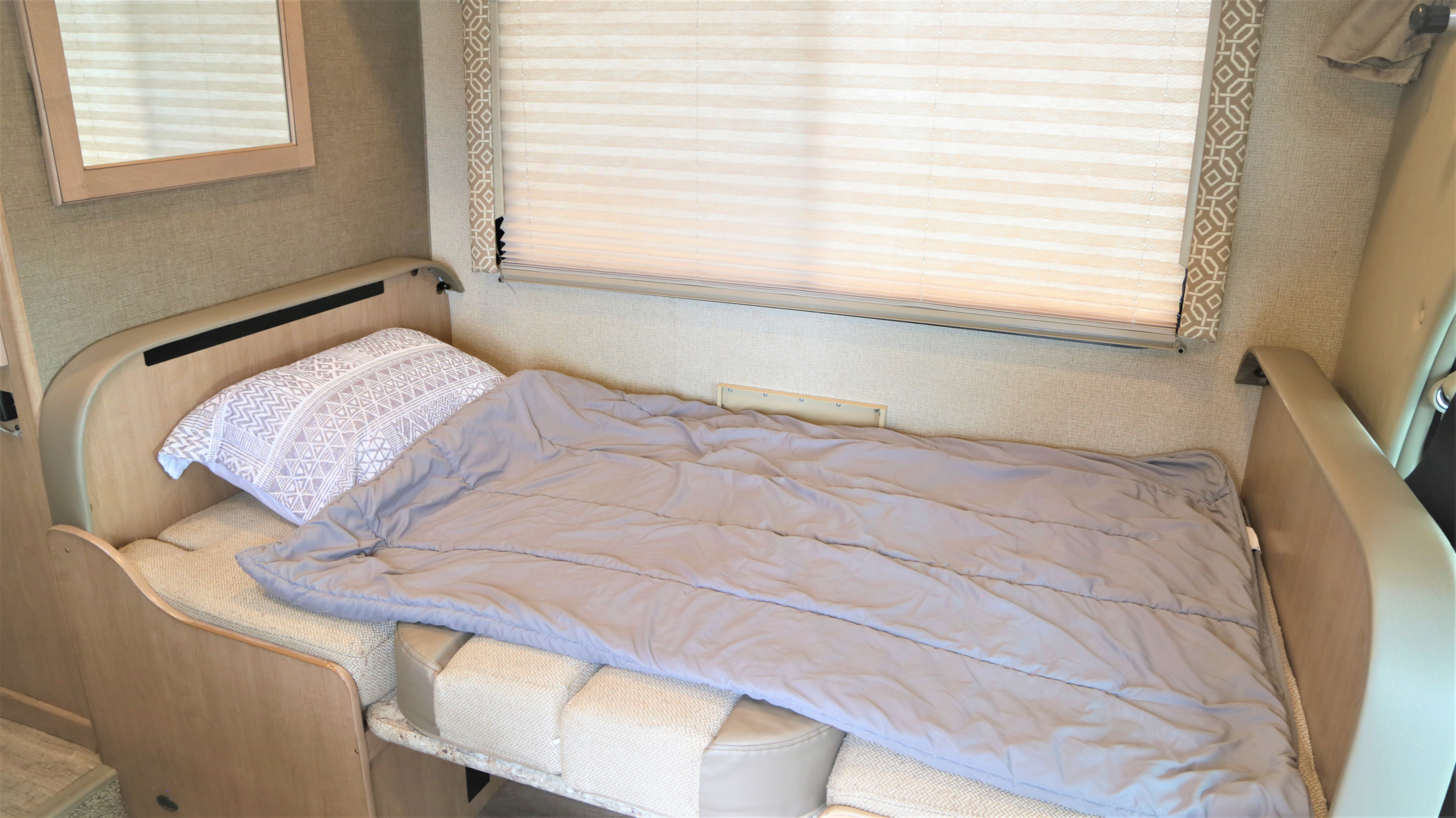 Cozy RV rental interior showing a bed made up with a gray comforter, patterned pillow, and window blinds.. Thor Freedom Elite 2020