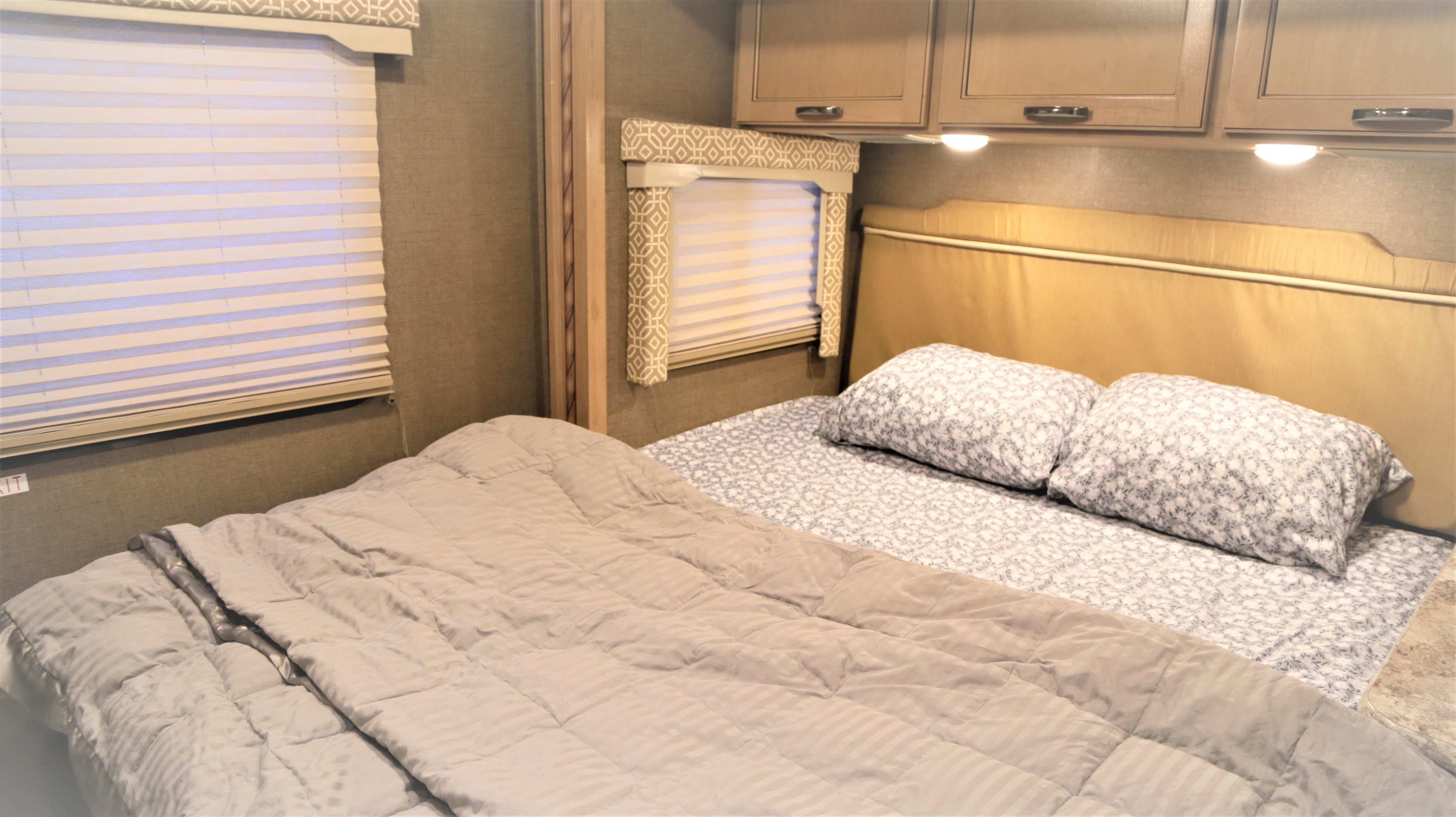 Cozy rv rental bedroom interior with a soft bed, patterned linens, windows, and overhead cabinets.. Thor Freedom Elite 2020