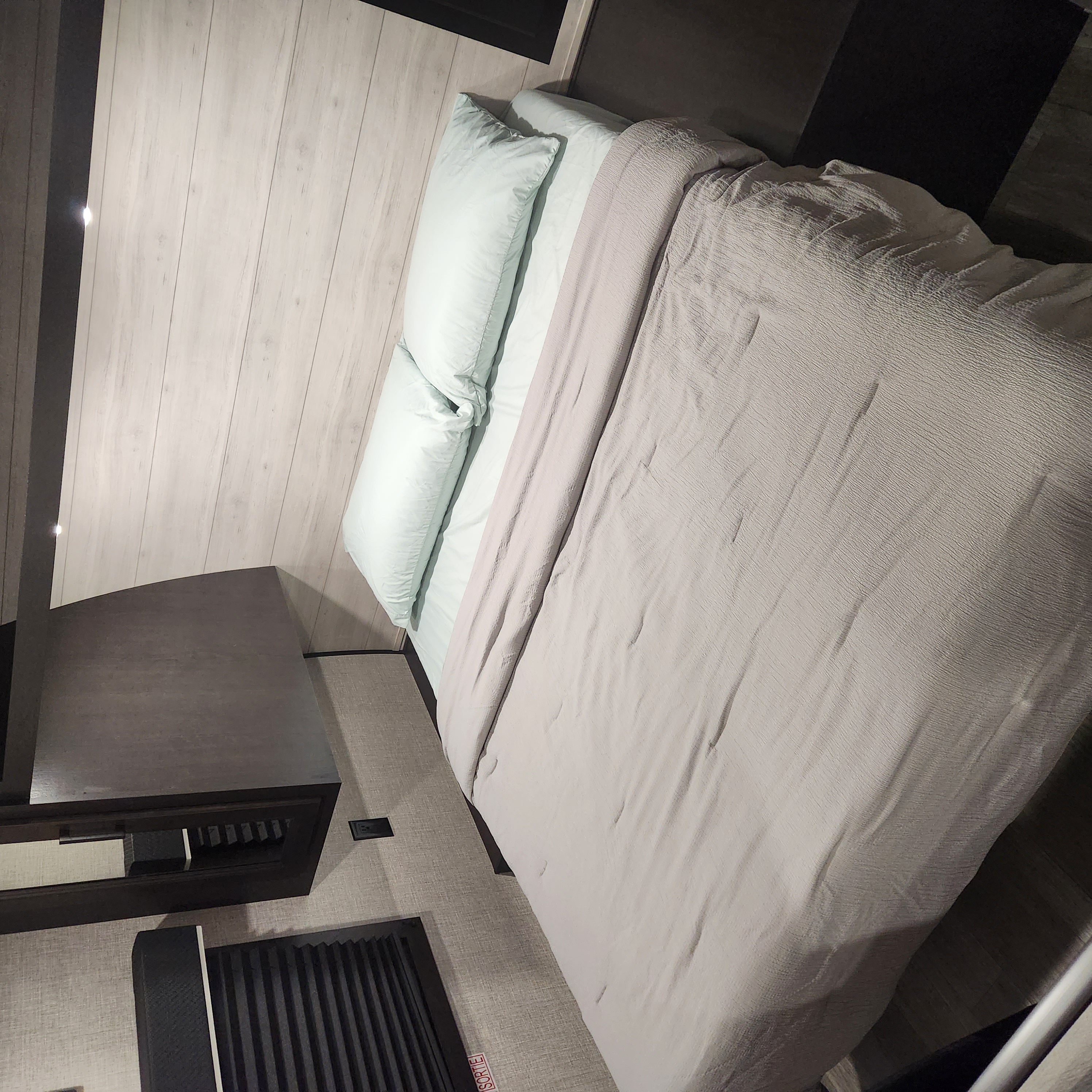 Cozy RV rental bedroom with light wood walls, a bed made with blue/grey bedding, and dark wood cabinetry.. Jayco 264bhw 2023