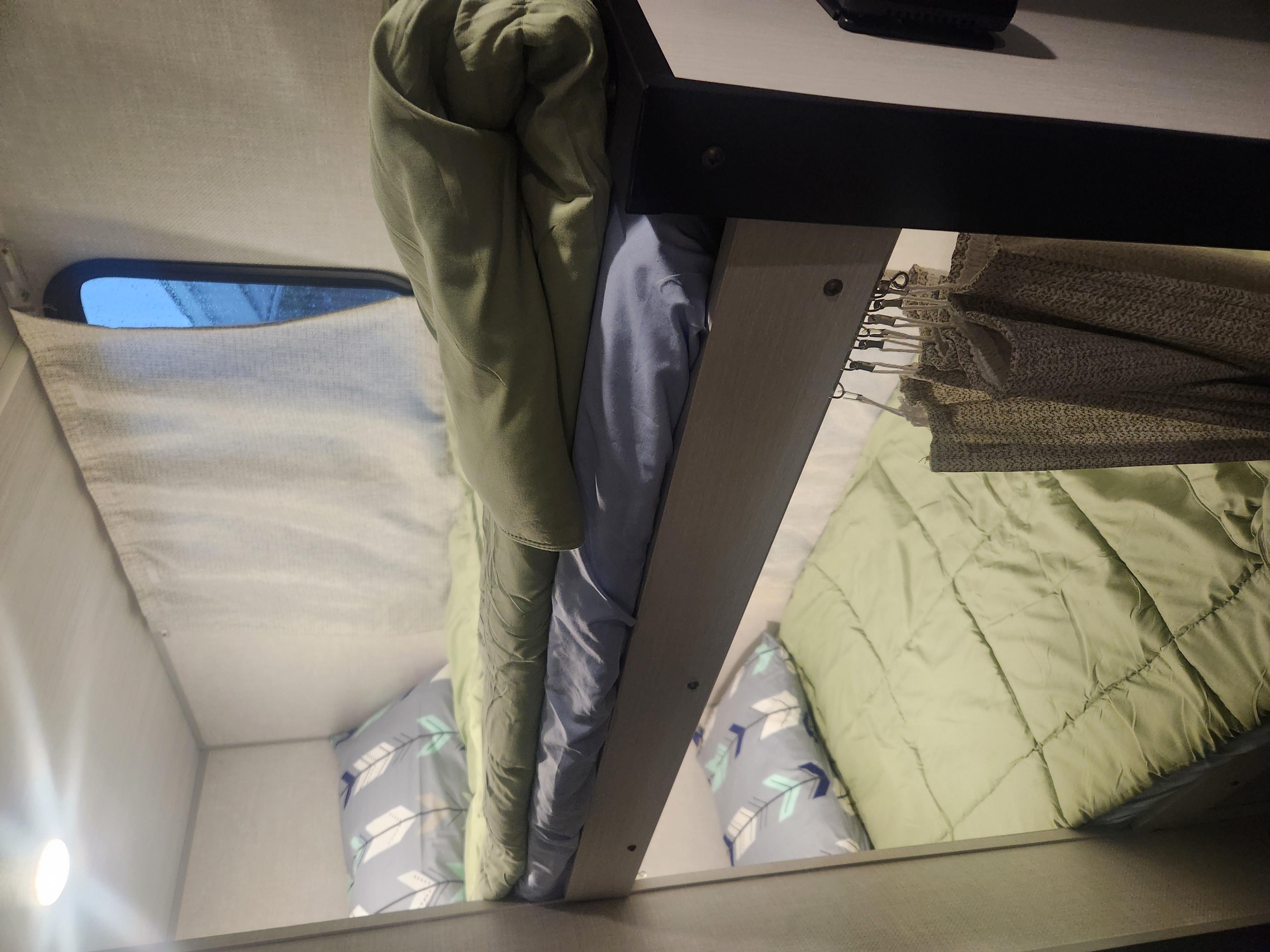 Inside an RV rental: cozy upper and lower bunk beds with green and patterned bedding, a side window, and curtains.. Forest River No Boundaries 2023