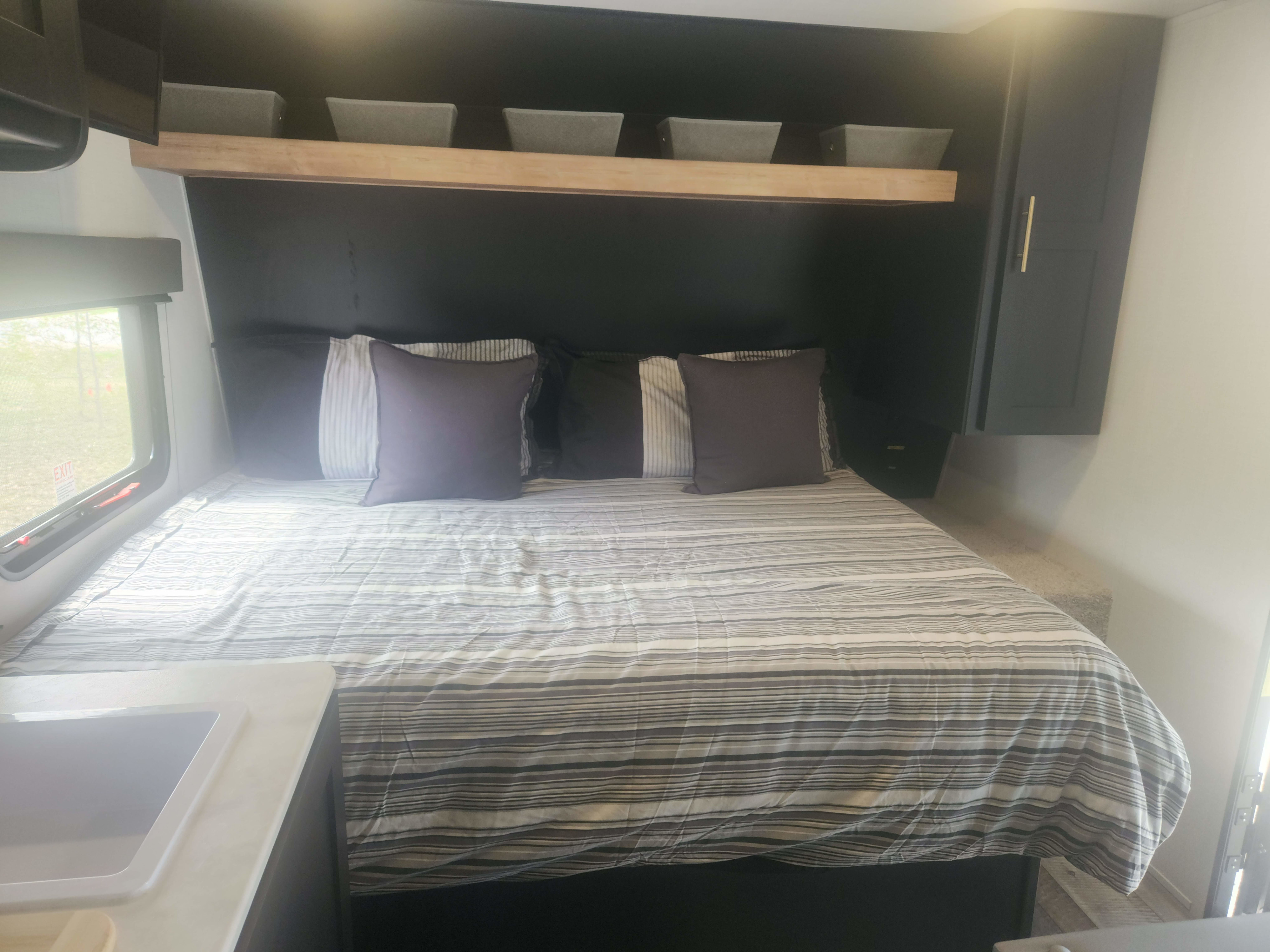 RV rental bedroom: cozy bed with striped comforter, overhead shelf with storage bins, and built-in cabinets for a functional space.. Keystone RV Springdale 2023