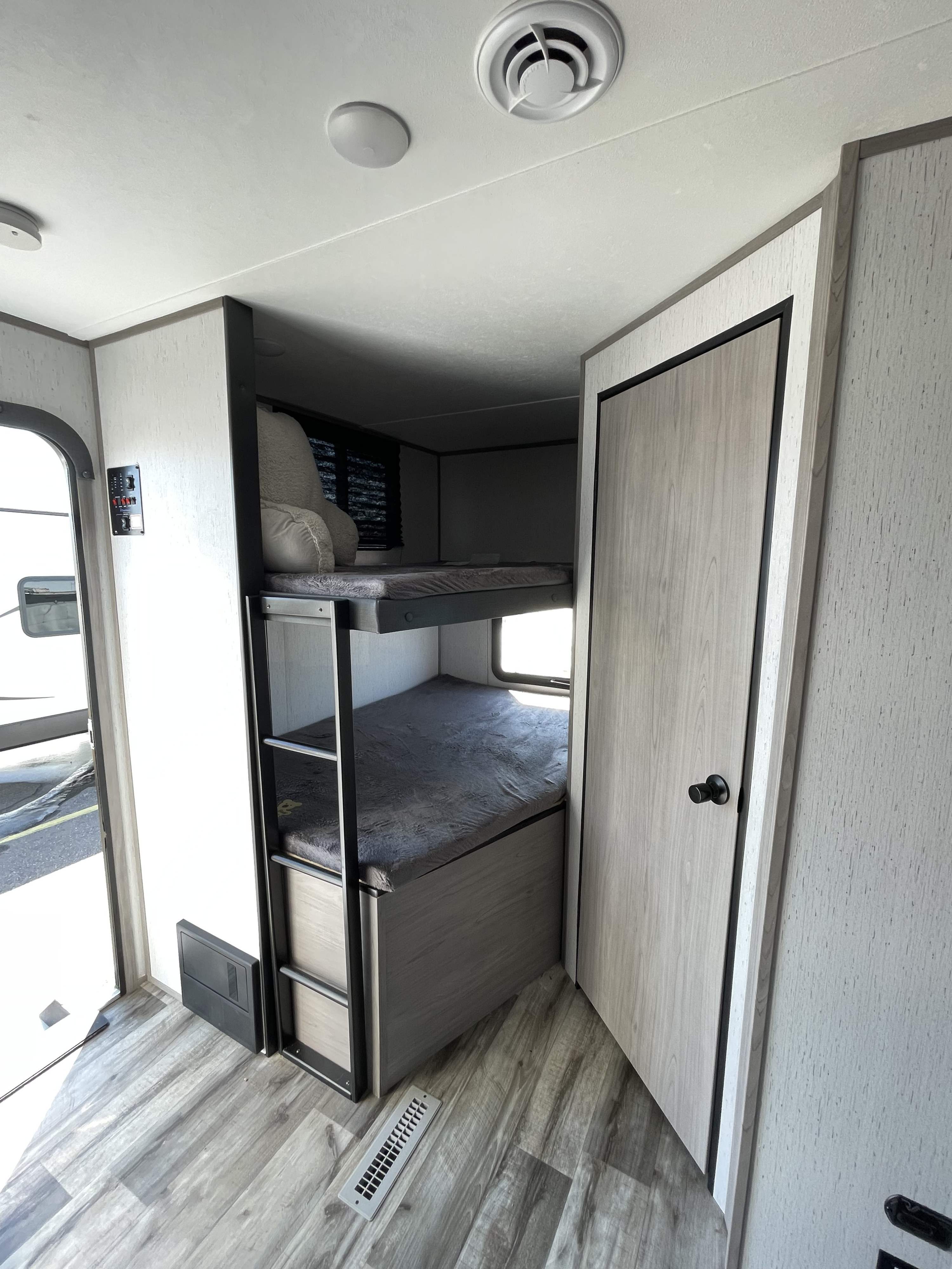 Cozy bunk beds and modern light wood interior in this inviting rv rental, featuring a ceiling vent and wall control panel.. Coleman Lantern 242BH 2022