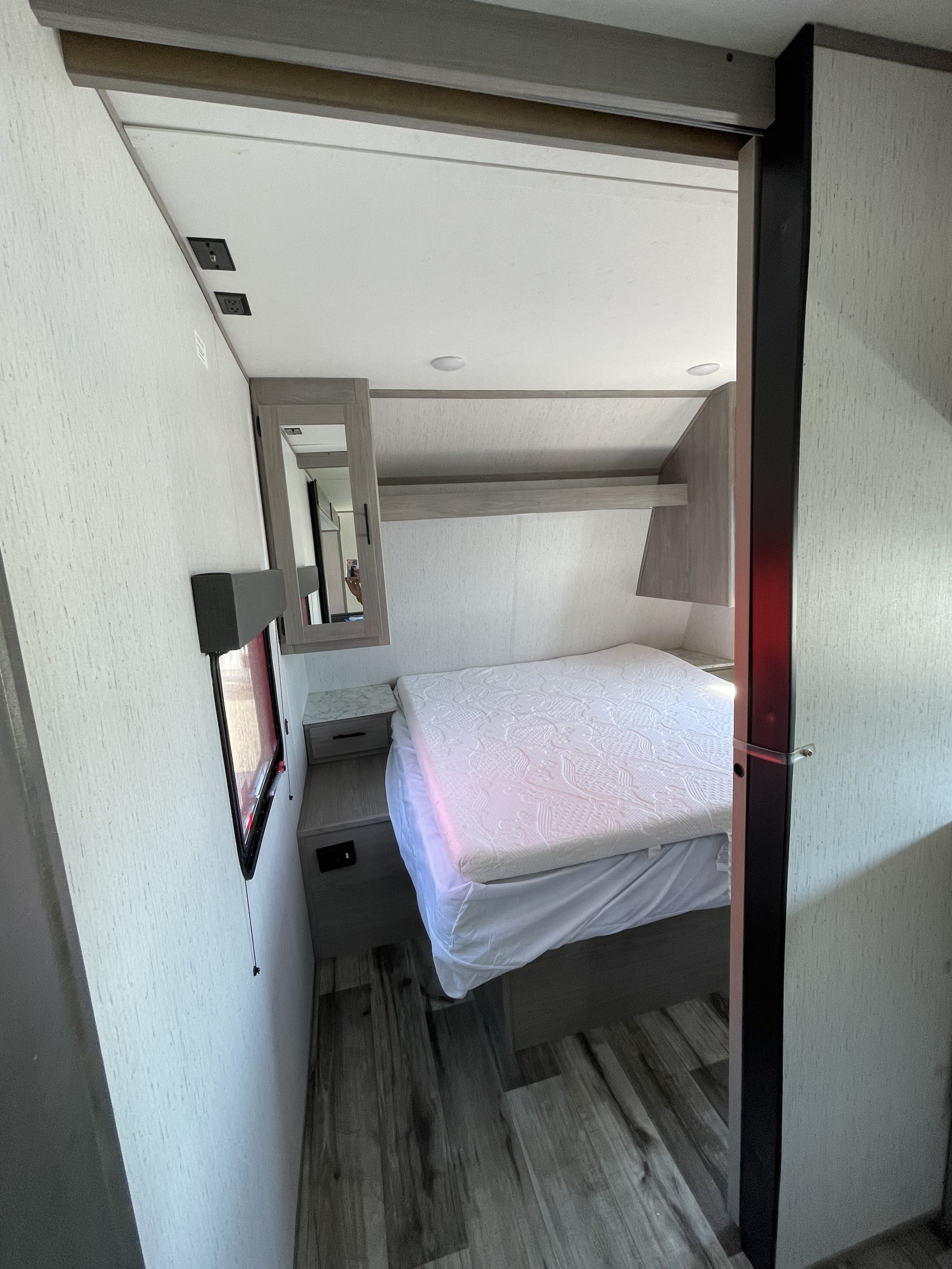 Modern RV rental bedroom featuring a neat bed, built-in storage, power outlets, and wood-look flooring.. Coleman Lantern 242BH 2022