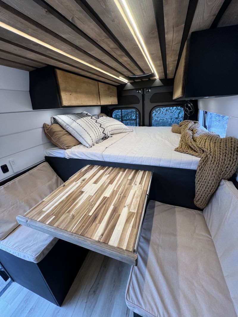 Inside a custom RV rental: a cozy bed, wooden ceiling with LED lights, and. Dodge Ram Promaster 2500 2022