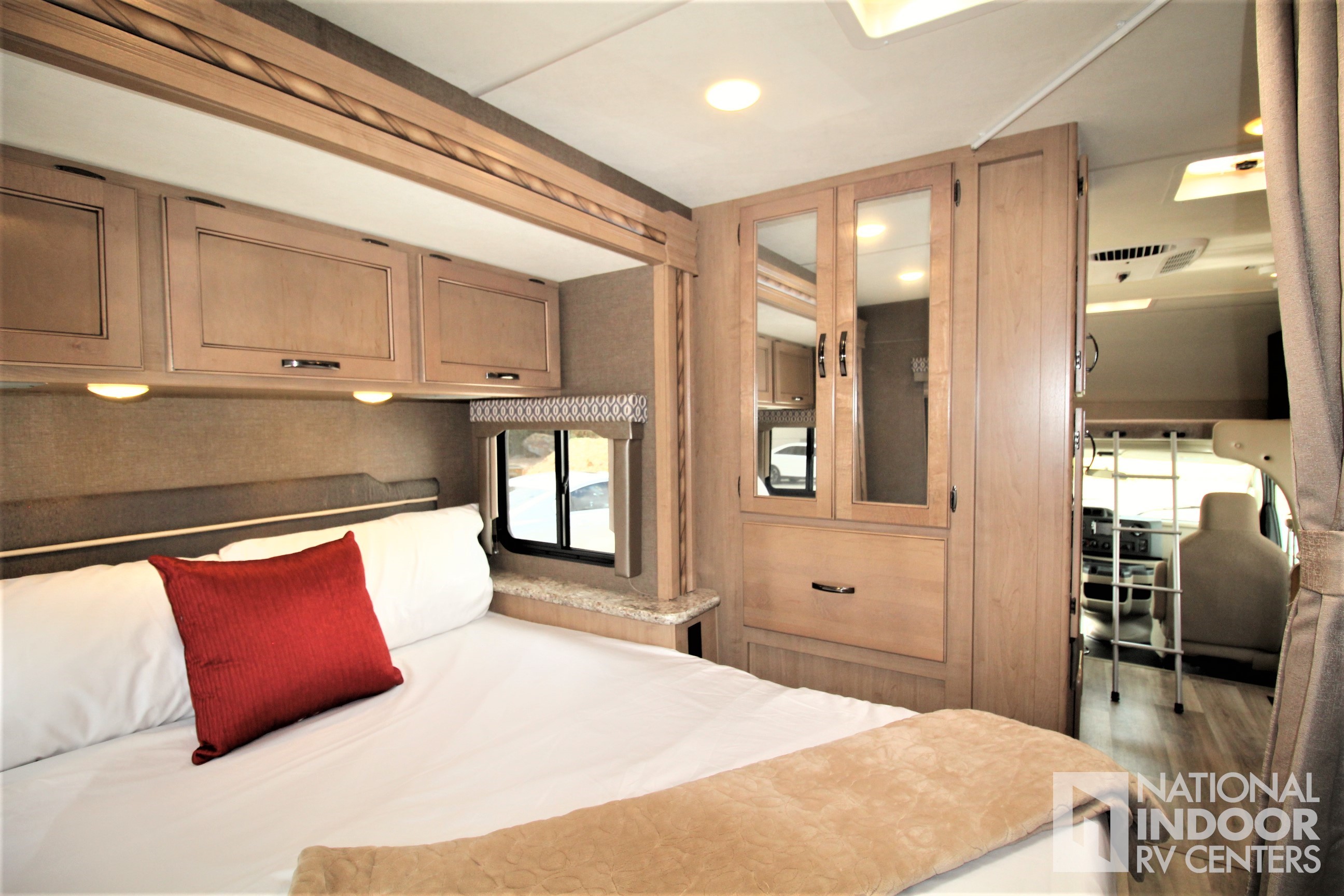 Inside an RV rental: cozy bedroom with light wood cabinets, red pillow on white bed, mirrored wardrobe & driver's area view.. Thor Motor Coach Freedom Elite 2018