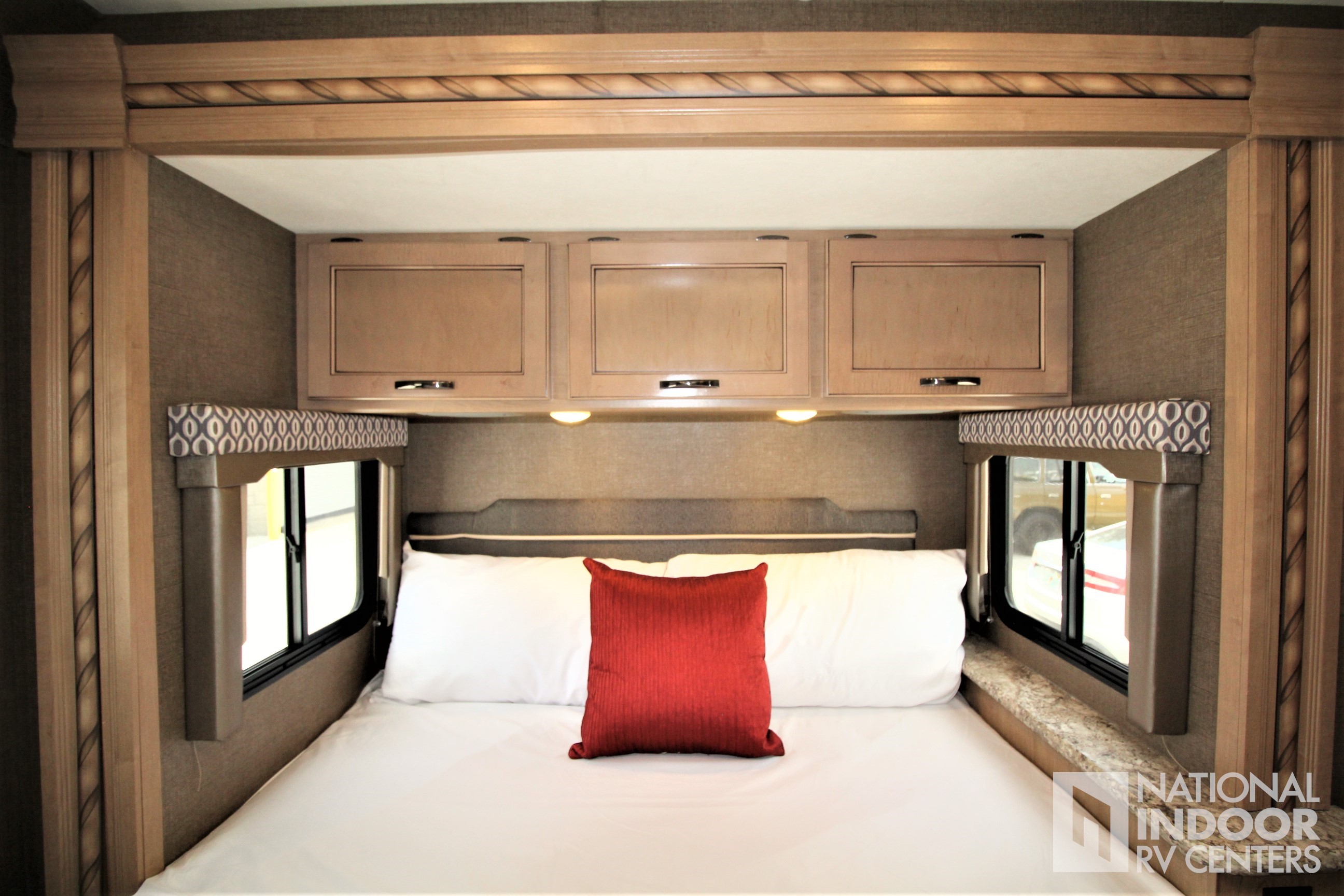 RV rental bedroom with a comfortable bed, white linens, red pillow, overhead cabinets, and windows for compact travel.. Thor Motor Coach Freedom Elite 2018