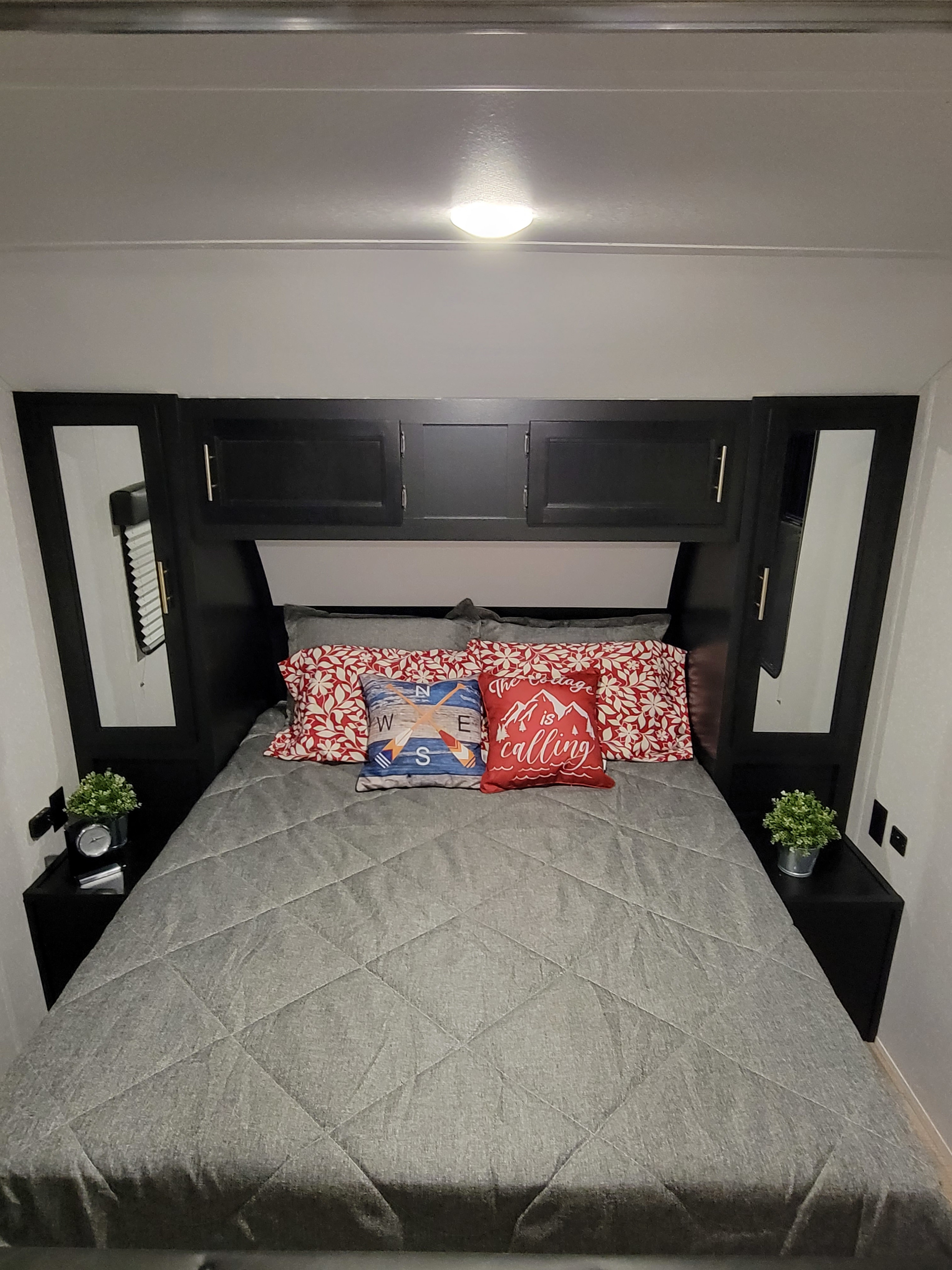 Inviting RV rental bedroom: comfy bed, patterned pillows, dark headboard with storage, and side tables.. Forest River Cherokee Grey Wolf 2022