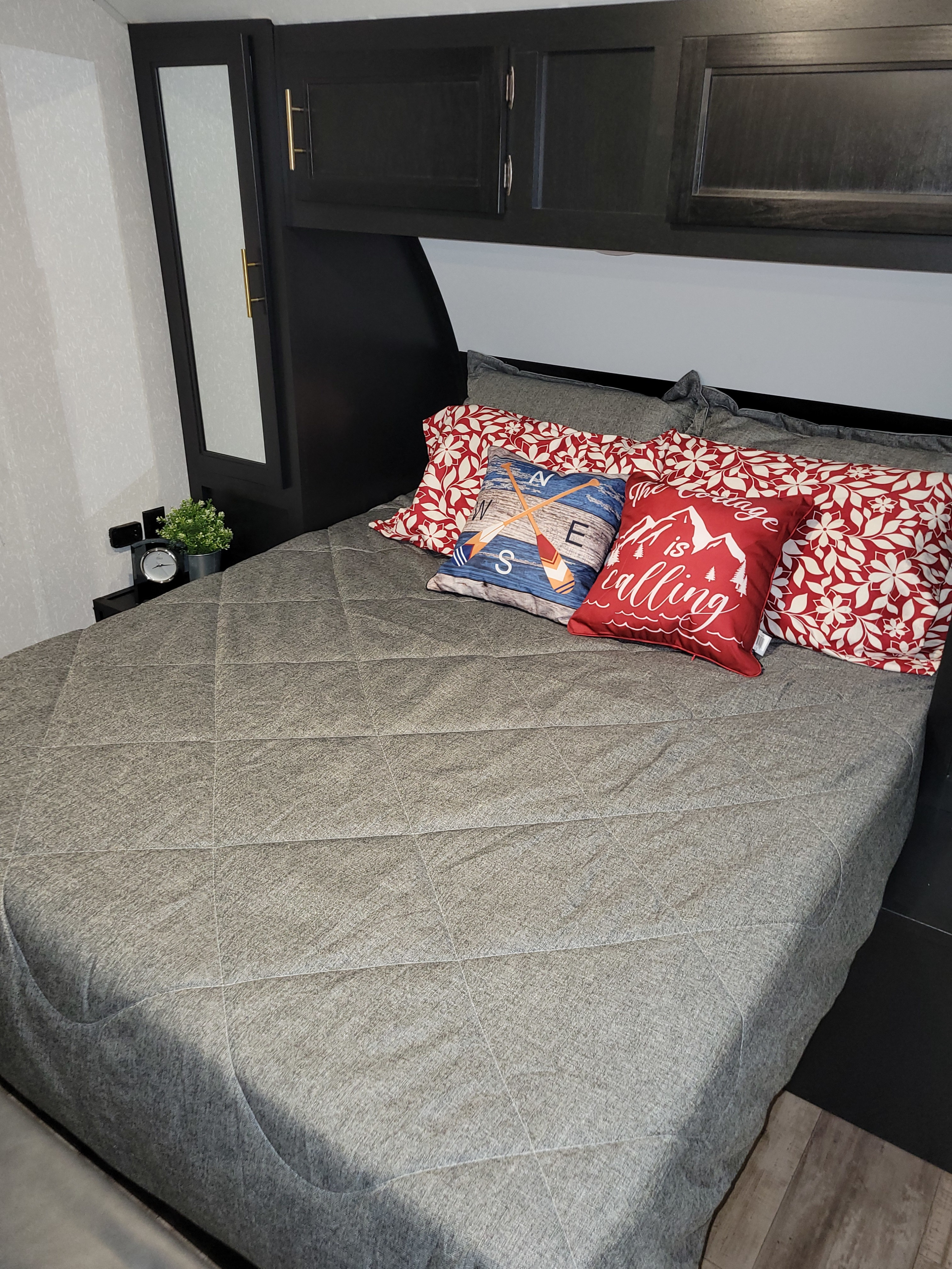 Cozy RV rental bedroom featuring a comfy bed with decorative pillows, compact storage, and a small nightstand.. Forest River Cherokee Grey Wolf 2022