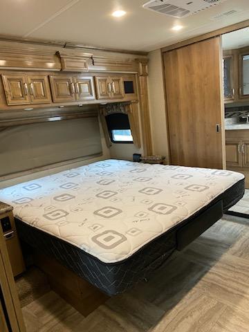 Spacious RV rental bedroom features a patterned mattress, overhead wood cabinets, and a sliding door.. Holiday Rambler Navigator 2019
