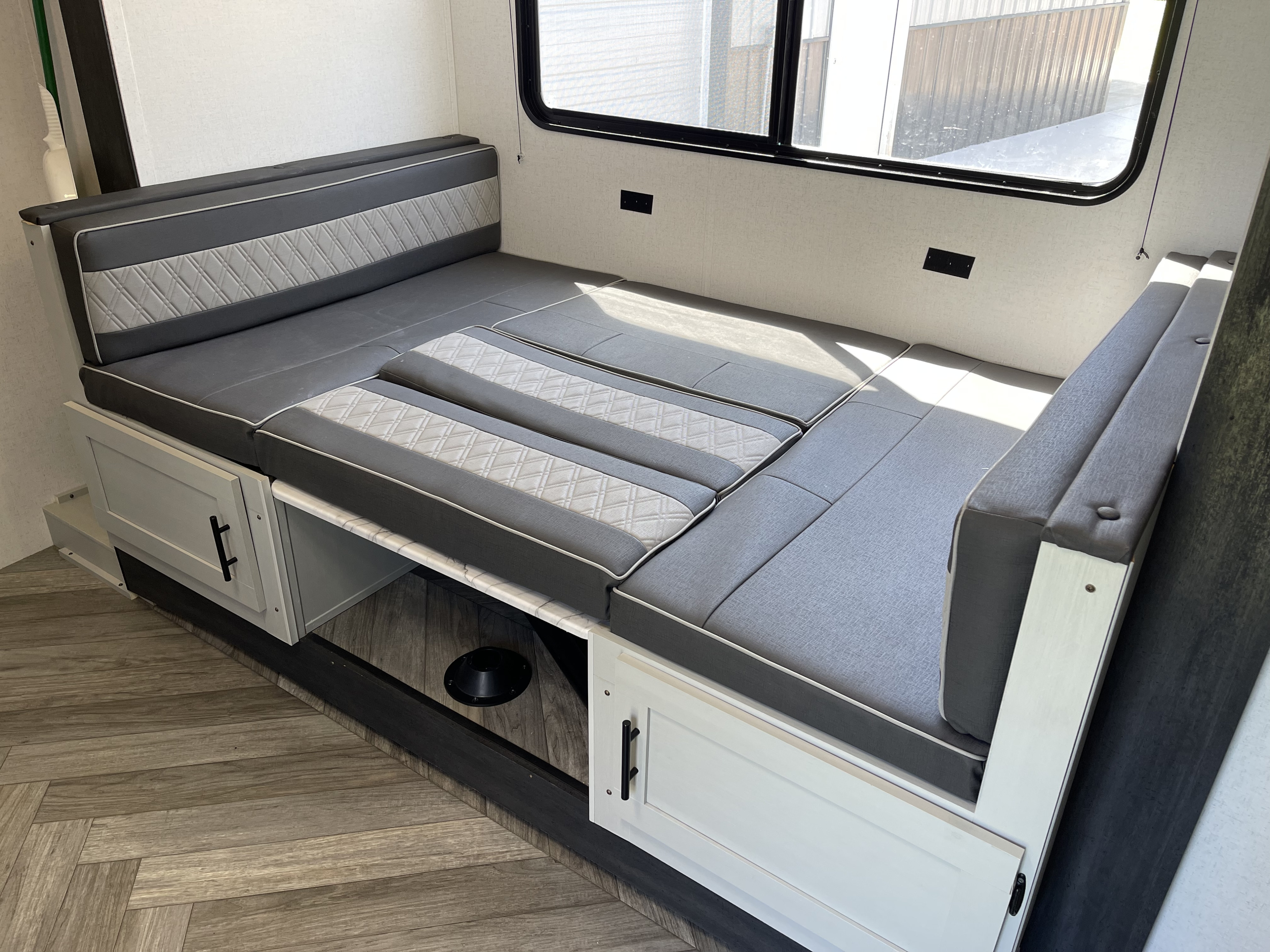 Compact RV rental dinette featuring gray and light gray patterned cushions, built-in storage, and a large window.. Forest River Salem FSX 2022