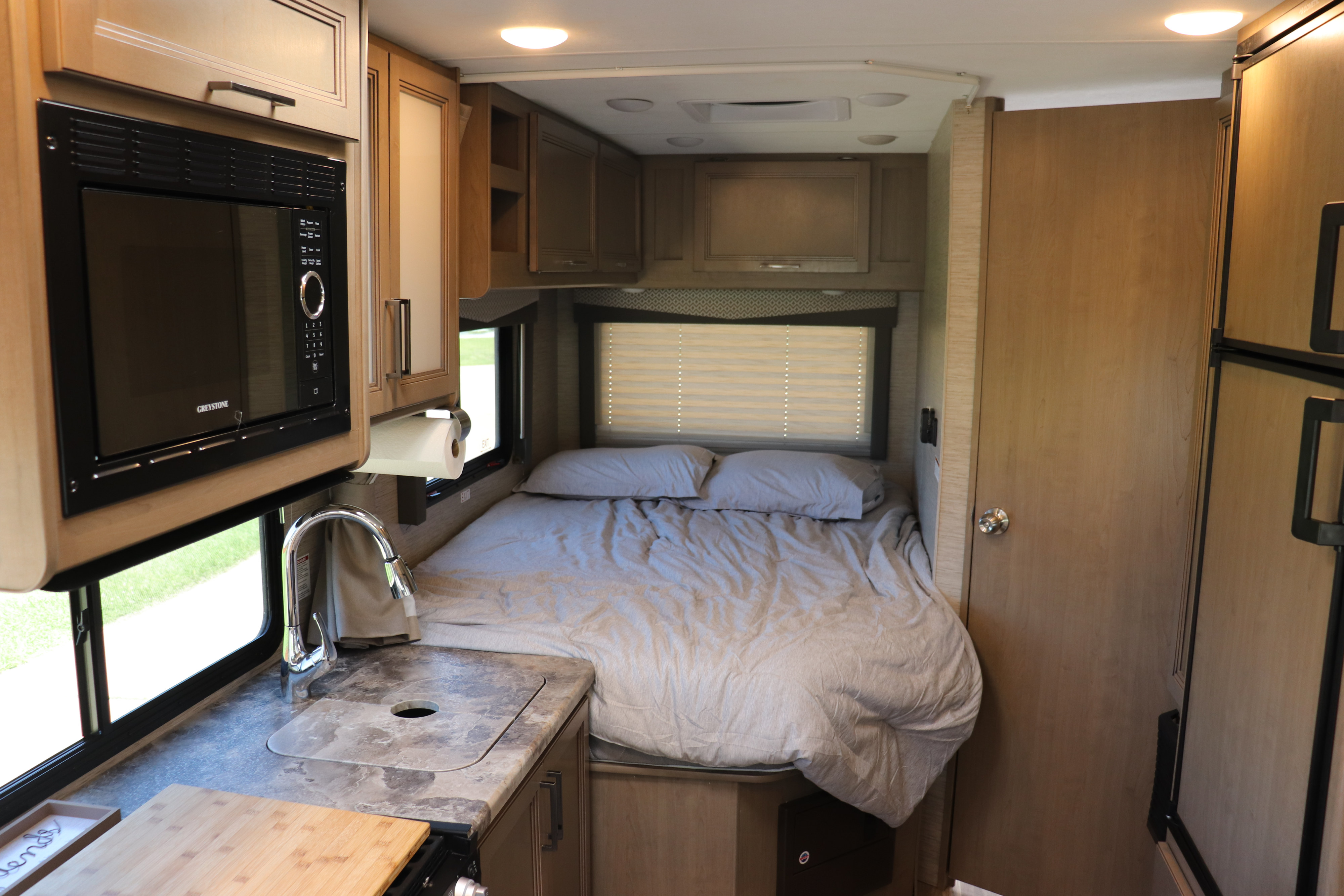 Inside an RV rental: a compact living space with a bed, kitchen sink, microwave, and refrigerator.. Thor Four Winds 2022