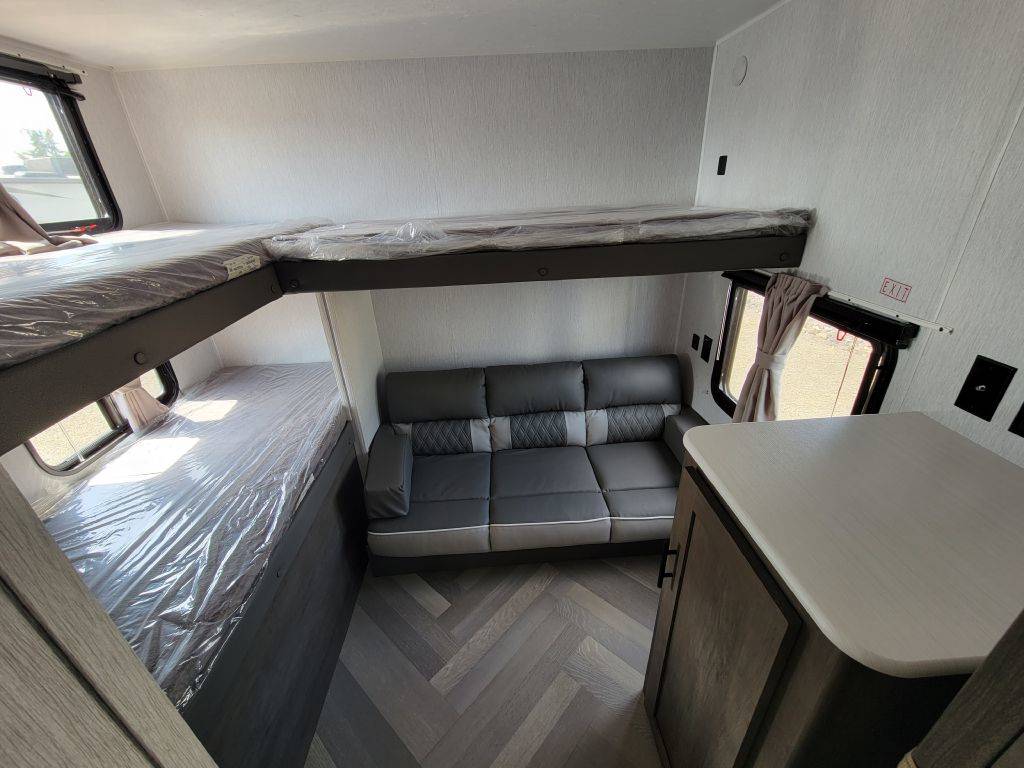 RV rental: Bunk beds with protective covers, a gray sofa, and a counter with storage. Ideal for family trips.. Forest River Evo 2023