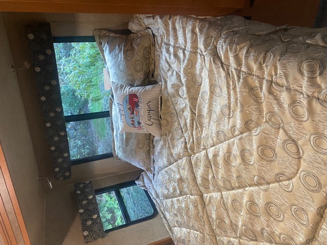 Cozy RV rental bedroom featuring a patterned bed, "Happy Camper" pillow, and a serene nature view from the windows.. Forest River Other 2017