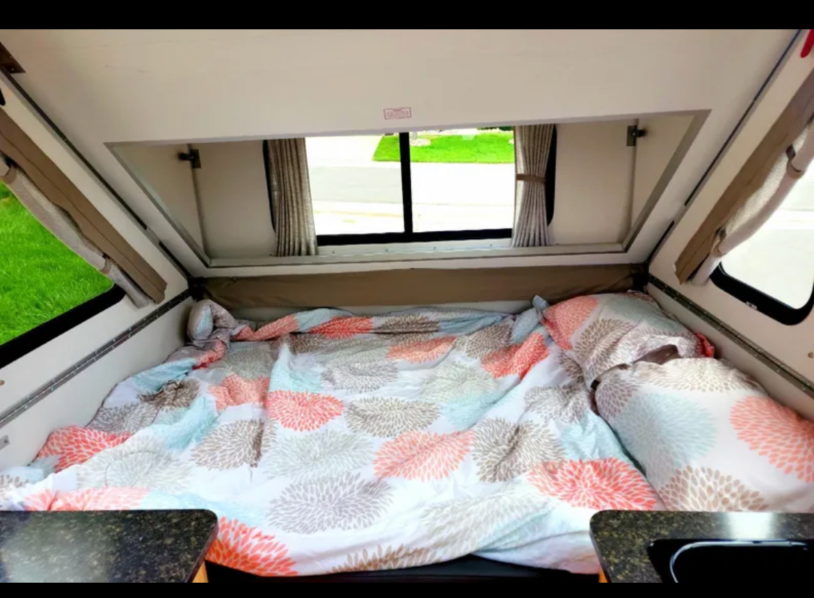 RV rental: Interior of a cozy pop-up camper featuring a bed with colorful floral bedding & bright windows.. A-liner Classic 2022