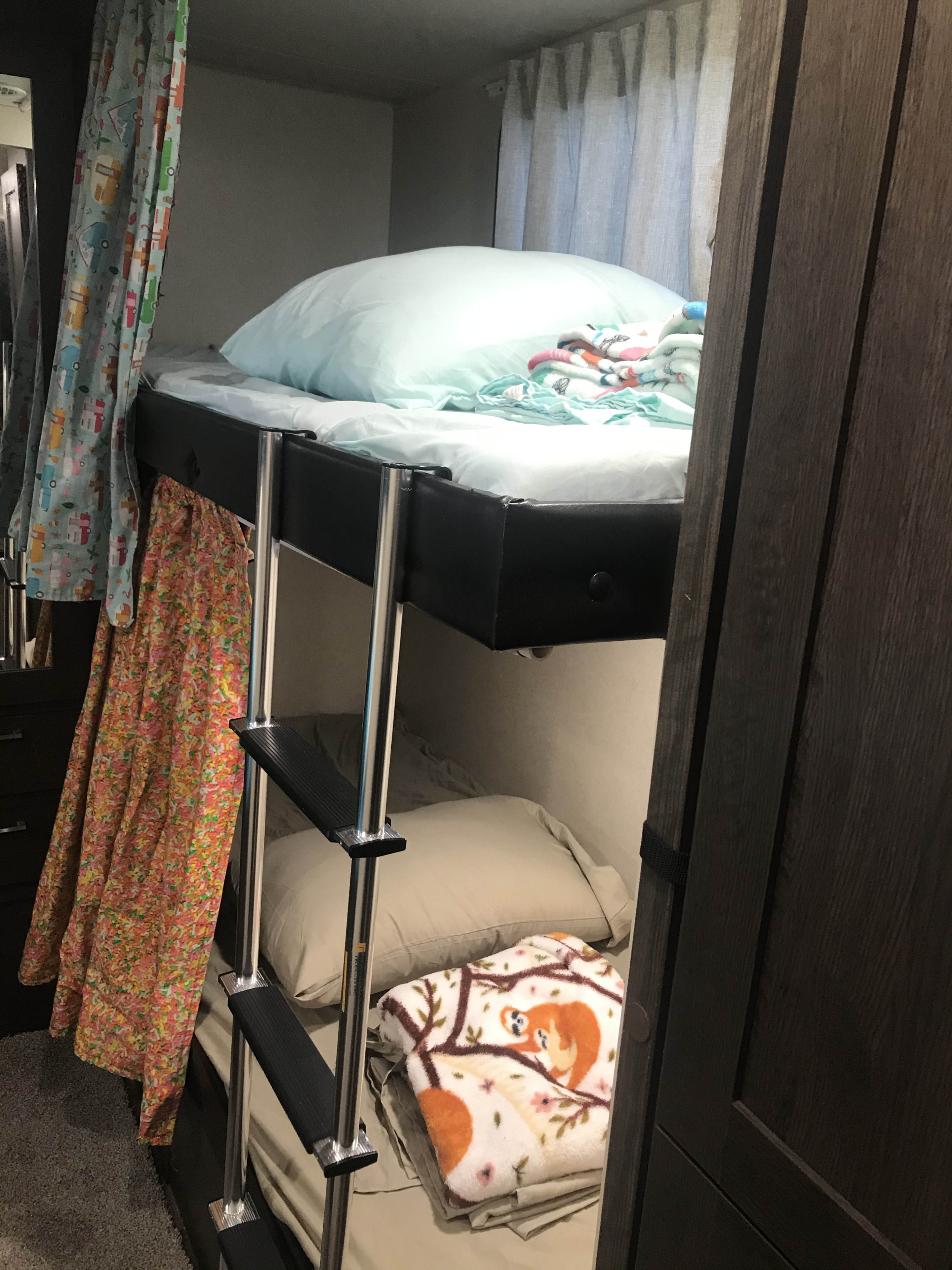 An RV rental sleeping area features cozy bunk beds with a ladder, colorful curtains, and soft blankets.. Forest River Wildwood X-Lite 2019