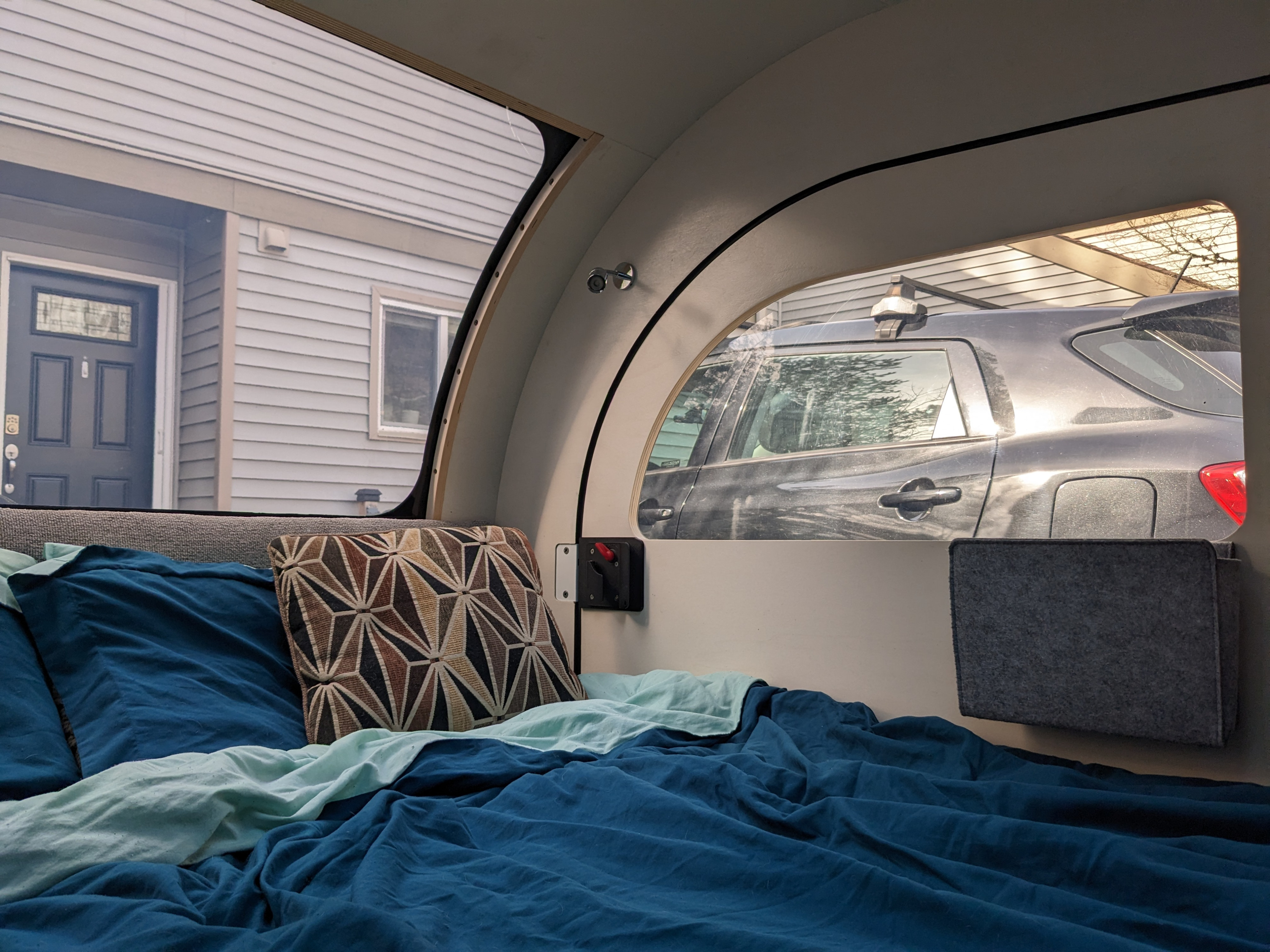 Cozy RV rental interior with a comfortable bed and window views of a house and SUV outside.. Droplet Travel Trailer 2022