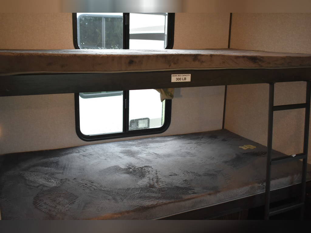 An RV rental's interior bunk beds. Two mattresses, windows, and a top bunk 300 LB capacity tag are visible.. Forest River Surveyor 2021
