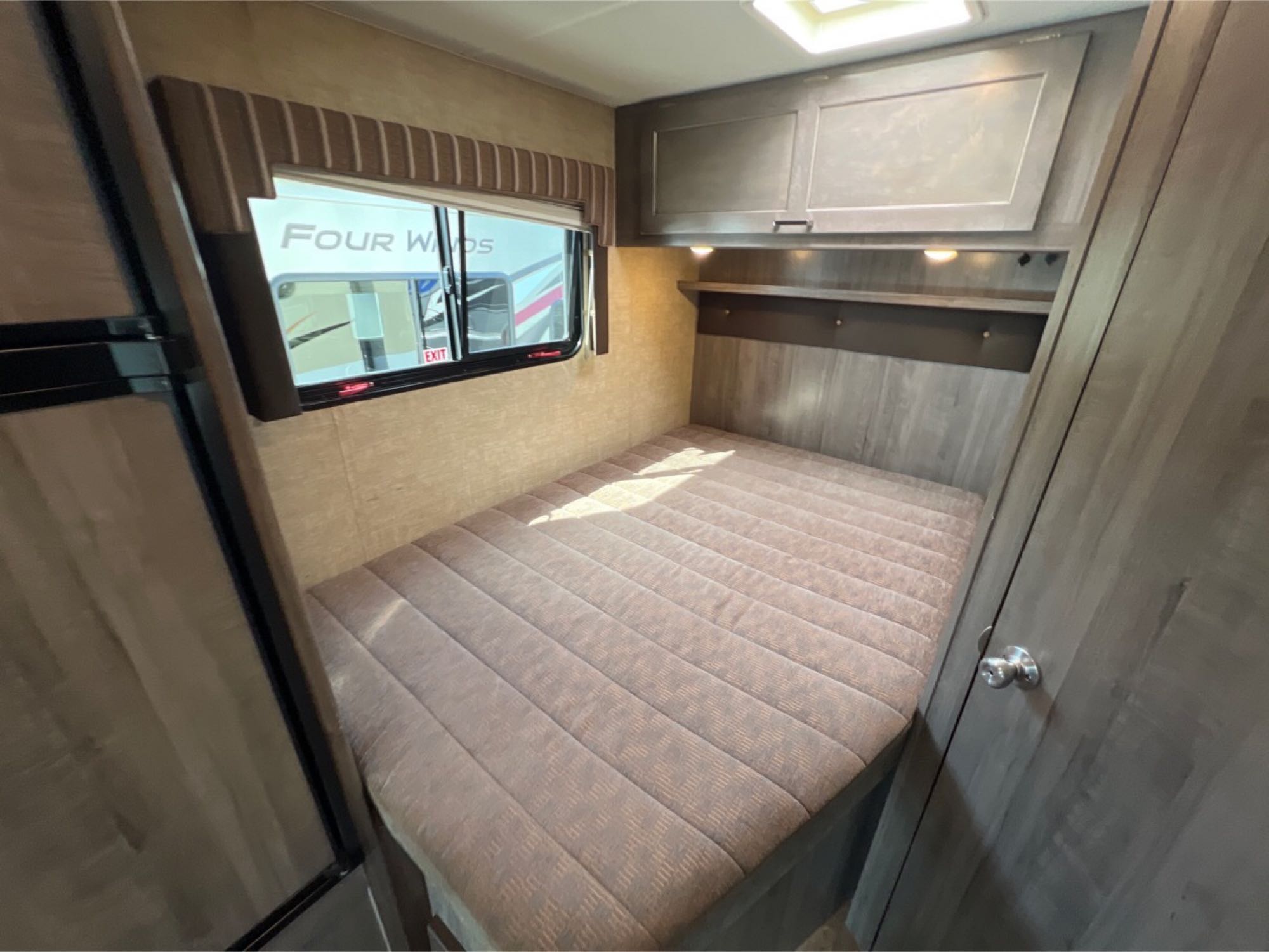 Cozy RV rental bedroom with a quilted bed, window view, and overhead cabinets for storage.. Winnebago Minnie Winnie 2019
