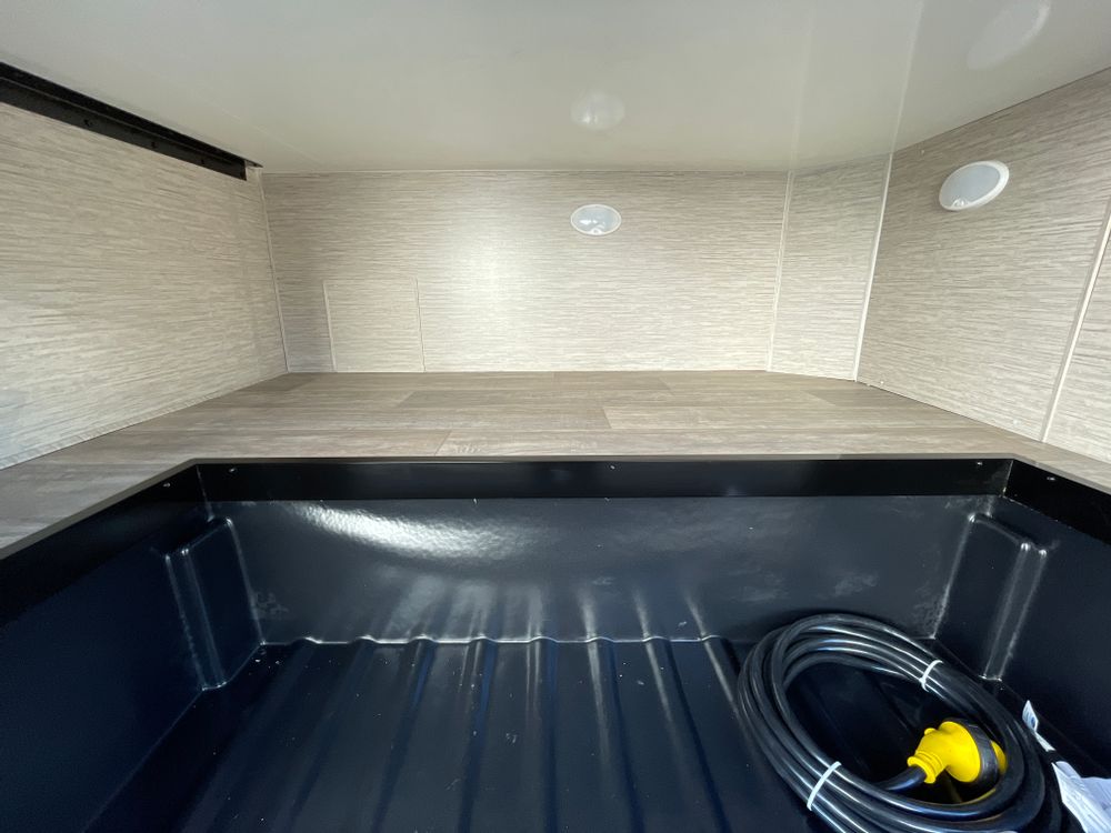 RV rental: Spacious interior with a raised bed/storage platform above a deep black cargo bin holding an electrical cord.. Thor Coleman 2023