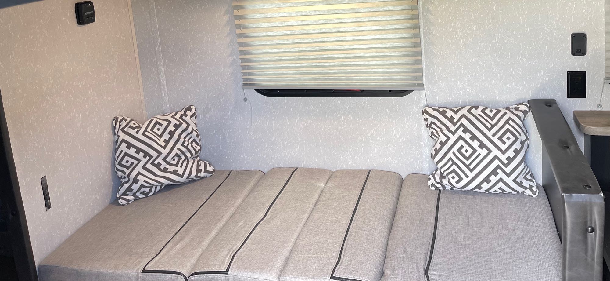 Inside an RV rental: a flexible seating area with grey cushions converts to a bed. Includes decorative pillows and a window with blinds.. Forest River Cherokee Wolf Pup Black Label 2021