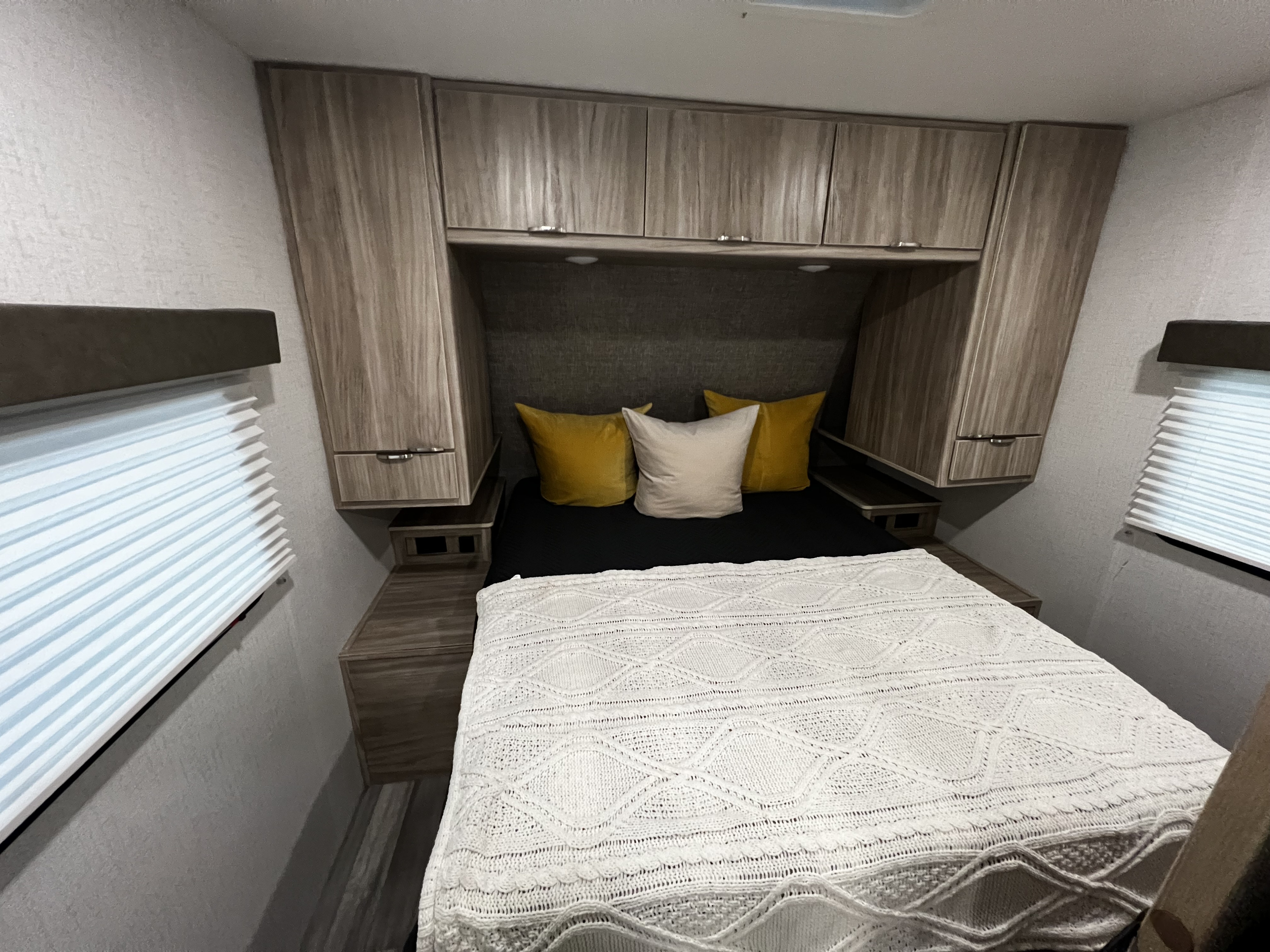 Compact and cozy RV rental bedroom featuring ample overhead cabinets, practical side nightstands, and pleated window blinds.. Winnebago Minnie Winnie 2023