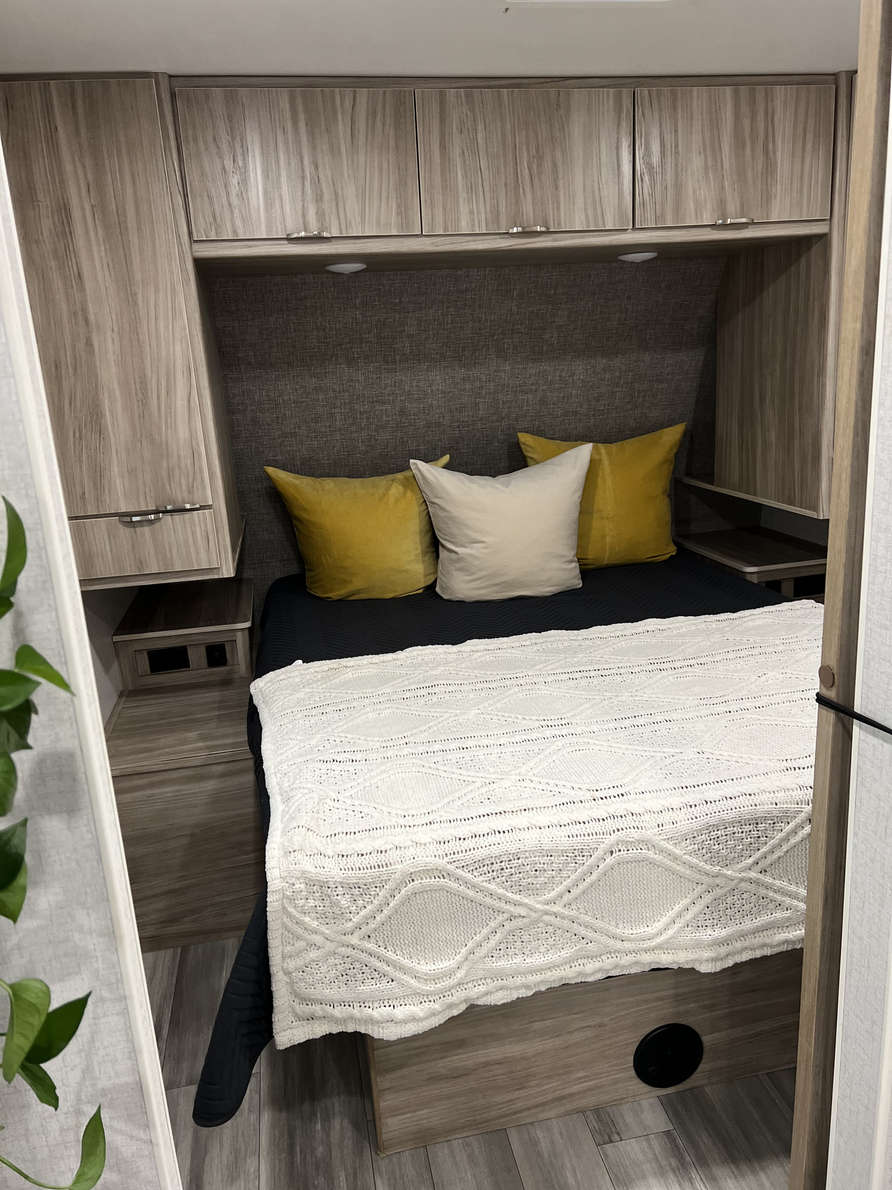 This inviting RV rental bedroom features a comfy bed with yellow pillows, overhead storage, and light wood finishes.. Winnebago Minnie Winnie 2023
