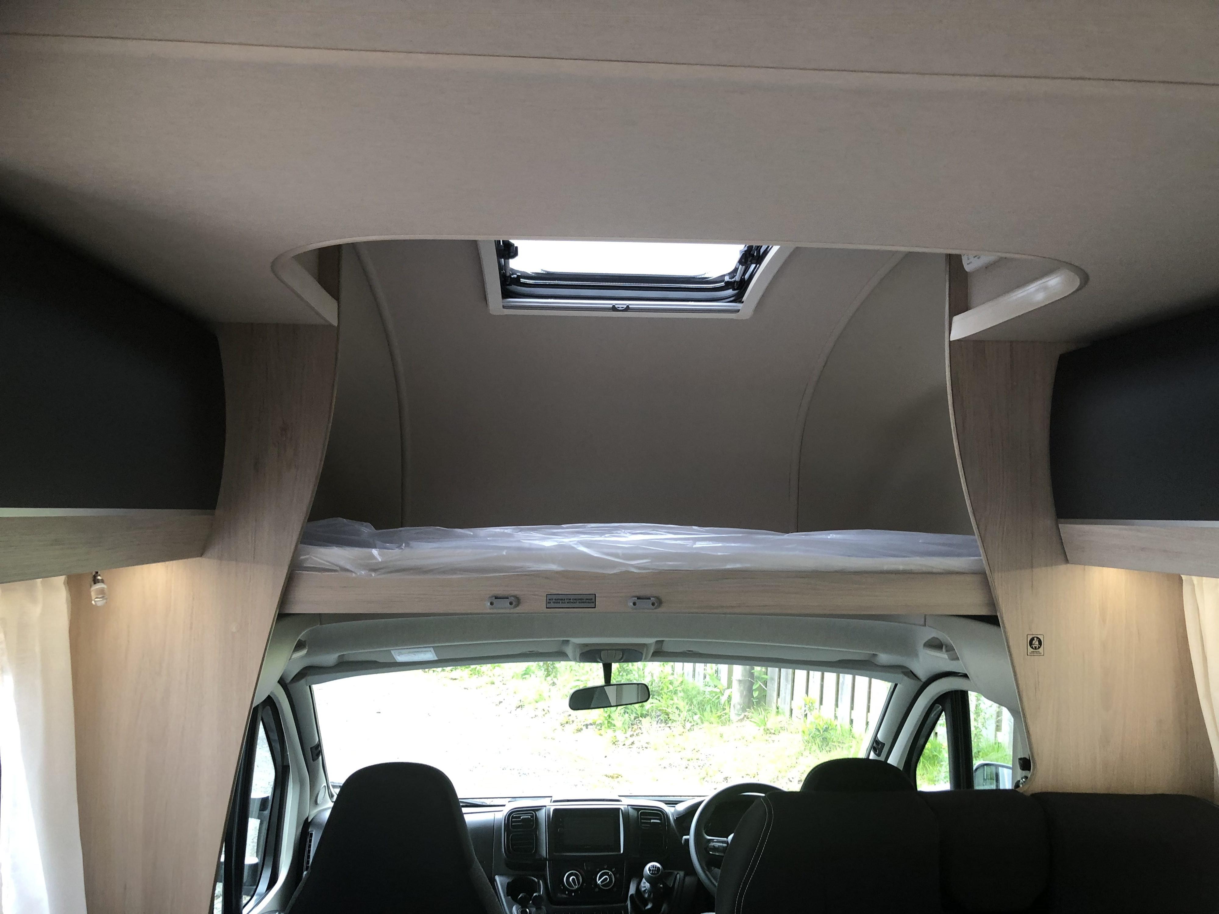 Inside this RV rental, see the front cab with an overhead bed wrapped in plastic, and a ceiling skylight.. Autotrail Expedition C72 2022