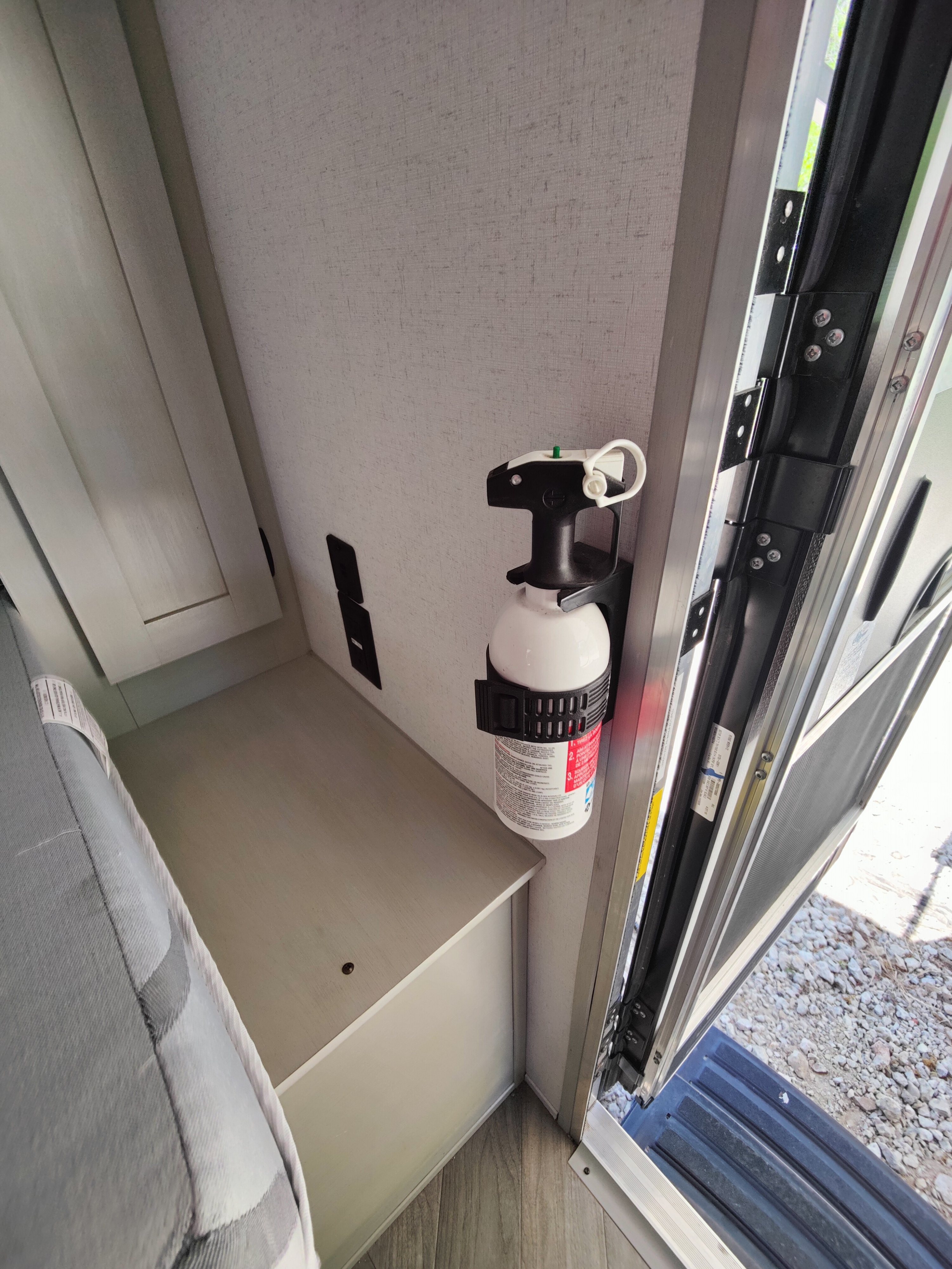 An RV rental interior shows a white fire extinguisher mounted by the entry, next to built-in storage and a bed.. Forest River Wildwood FSX 2021
