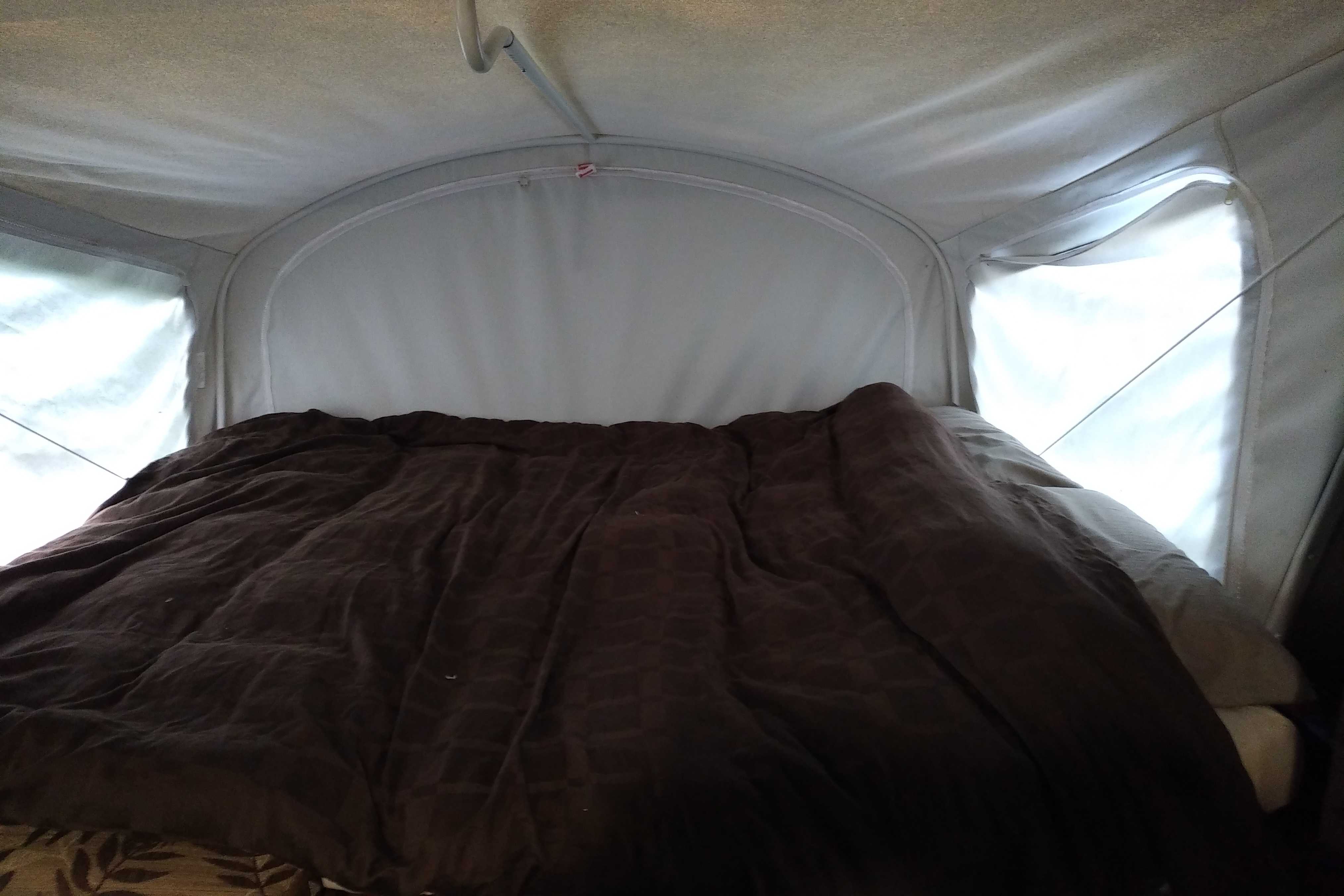 Cozy RV rental sleeping area with a dark comforter and light-filled pop-up tent windows.. Other Other 2015