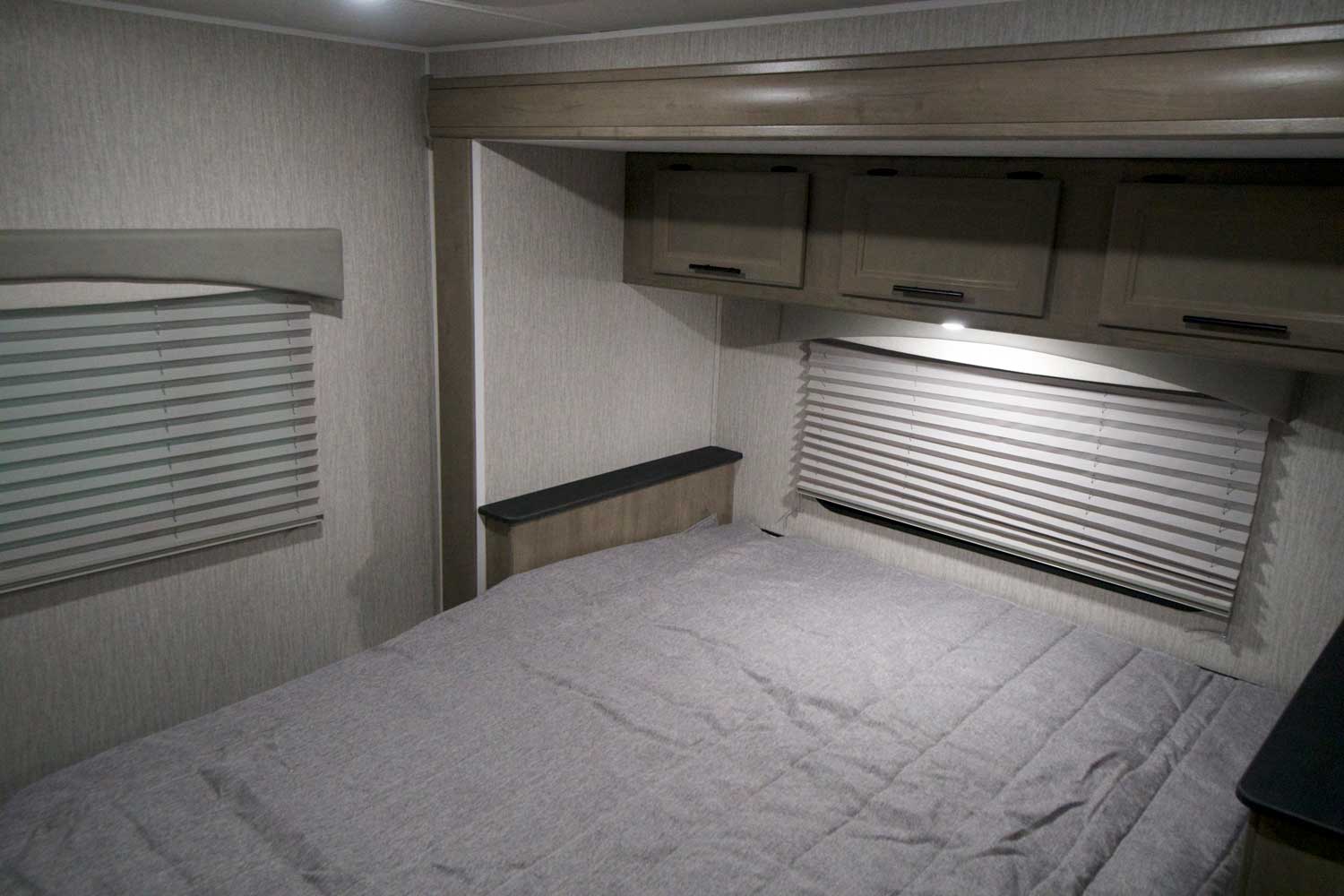 Comfortable RV rental bedroom with grey bed, overhead cabinets, and windows with blinds for cozy travel.. Forest River Coachmen Freelander 2022
