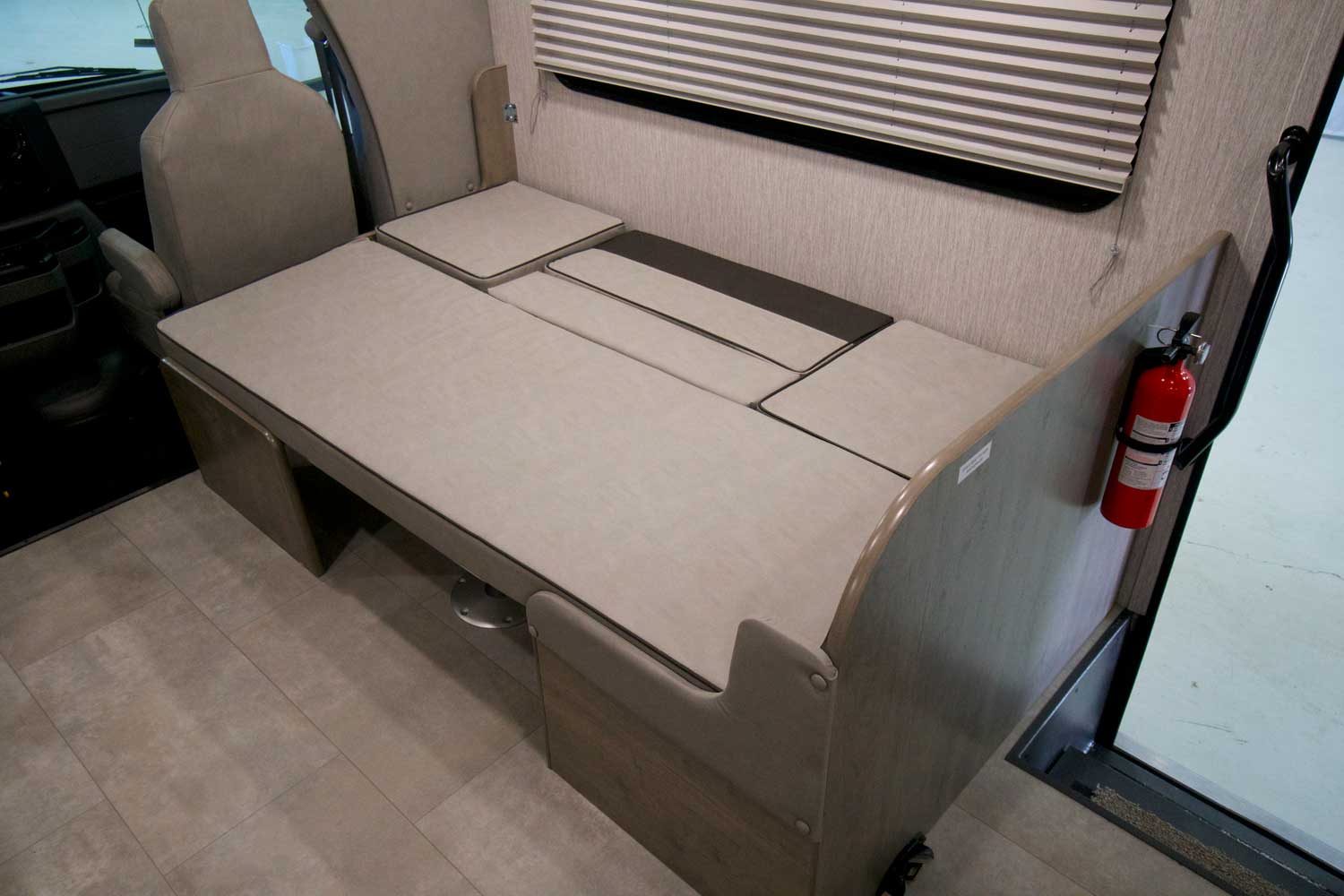 This RV rental features a flexible gray cushioned seating/bed area, window blinds, and a fire extinguisher for safety.. Forest River Coachmen Freelander 2022