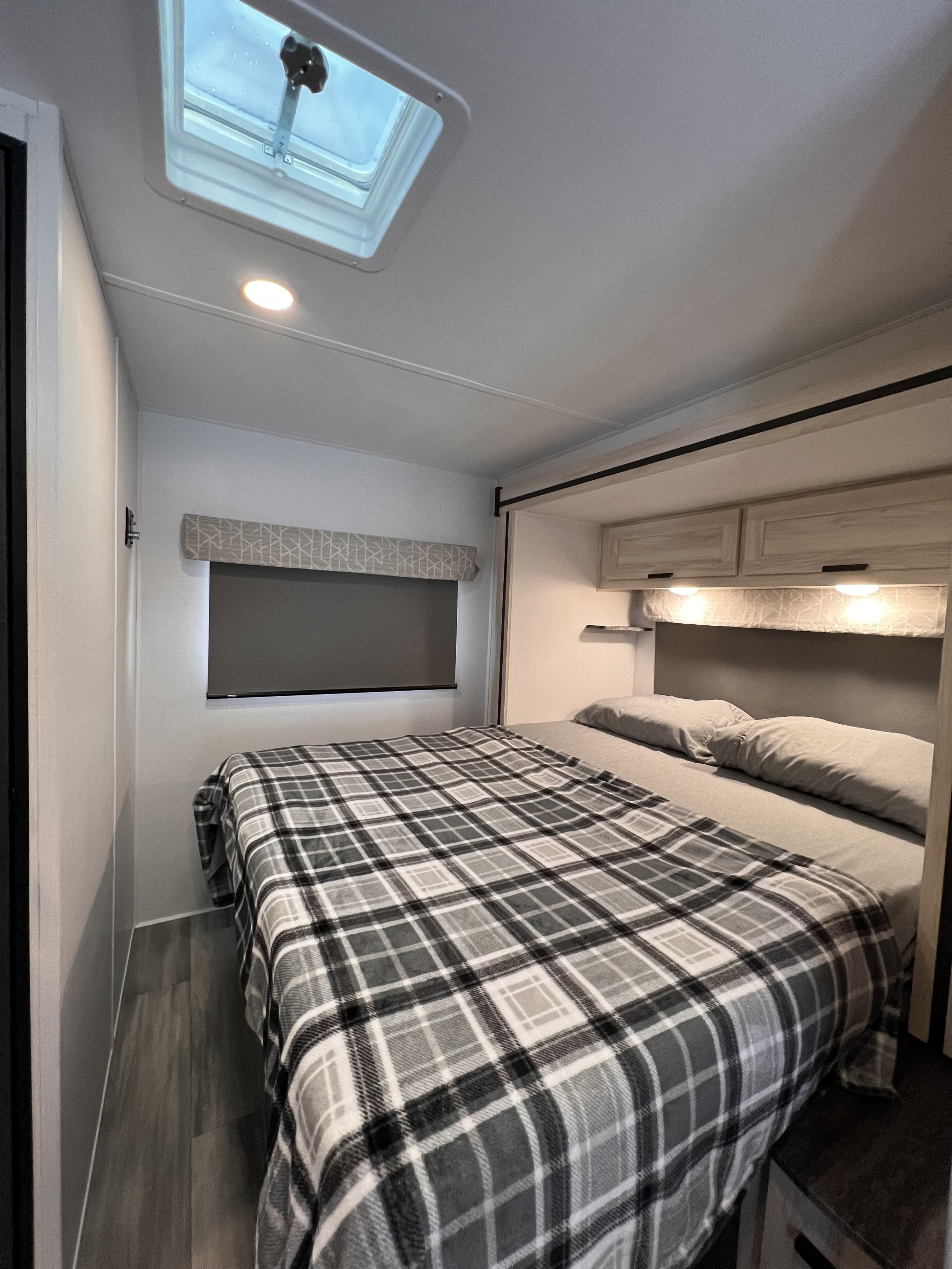 Comfortable RV rental bedroom featuring a plaid bed, overhead cabinets, and a skylight, showing a cozy interior.. Forest River Sunseeker 2024