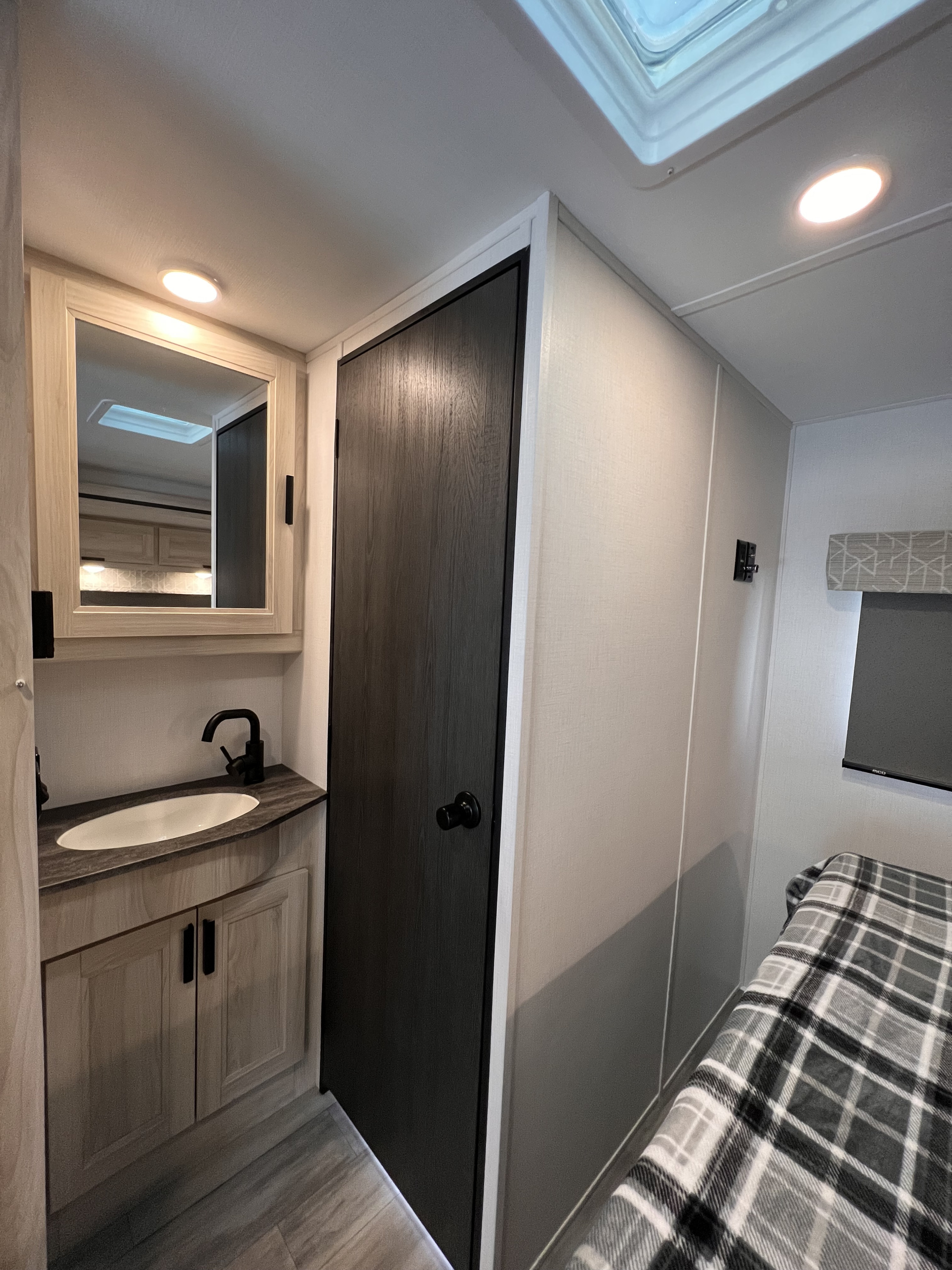 Cozy RV rental interior: vanity with sink/mirror, dark door, and bedroom with plaid blanket, TV. Ideal for travel.. Forest River Sunseeker 2024
