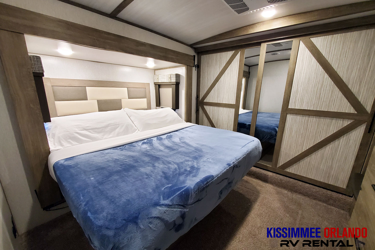 Comfortable RV rental bedroom featuring a full-size bed with a blue blanket and mirrored sliding closet doors.. Forest River Salem Hemisphere 2022