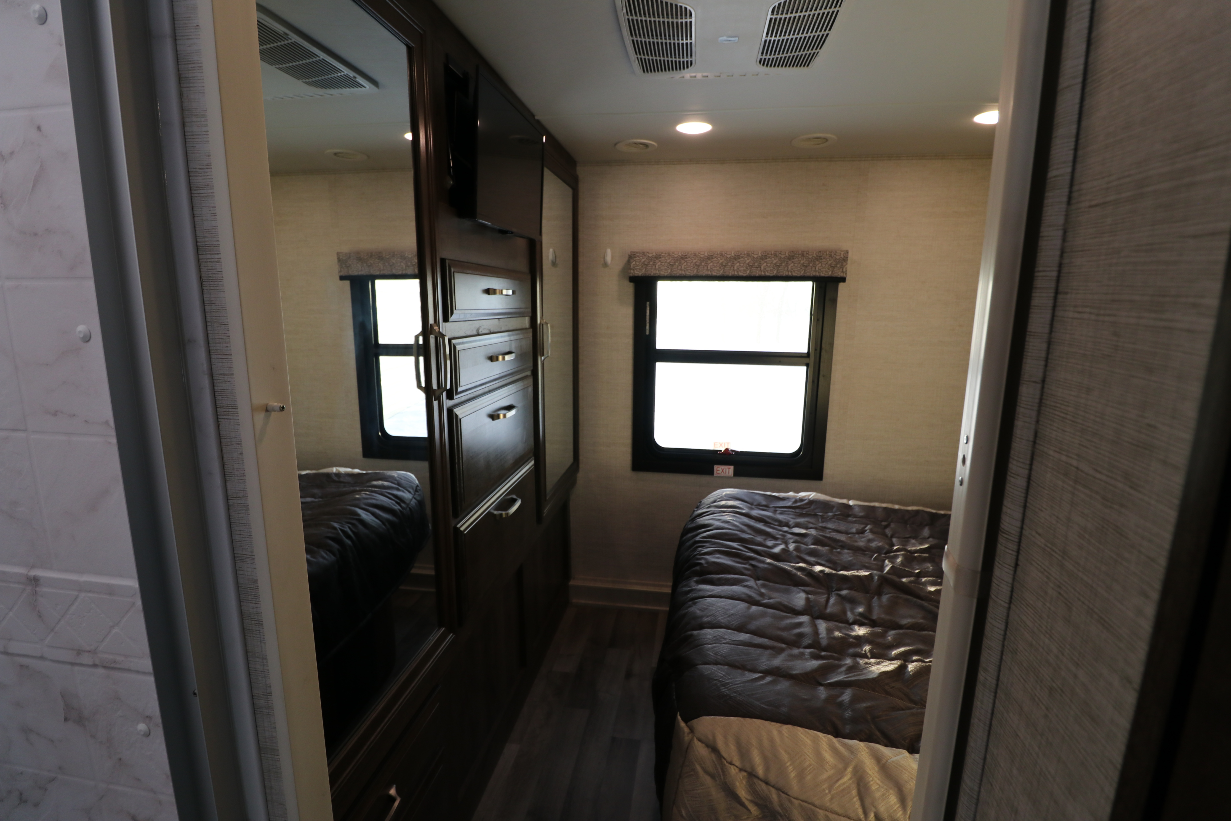 Inside a cozy RV rental bedroom: features a bed, mirrored wardrobe with TV, and bright windows.. Jayco Greyhawk 2021