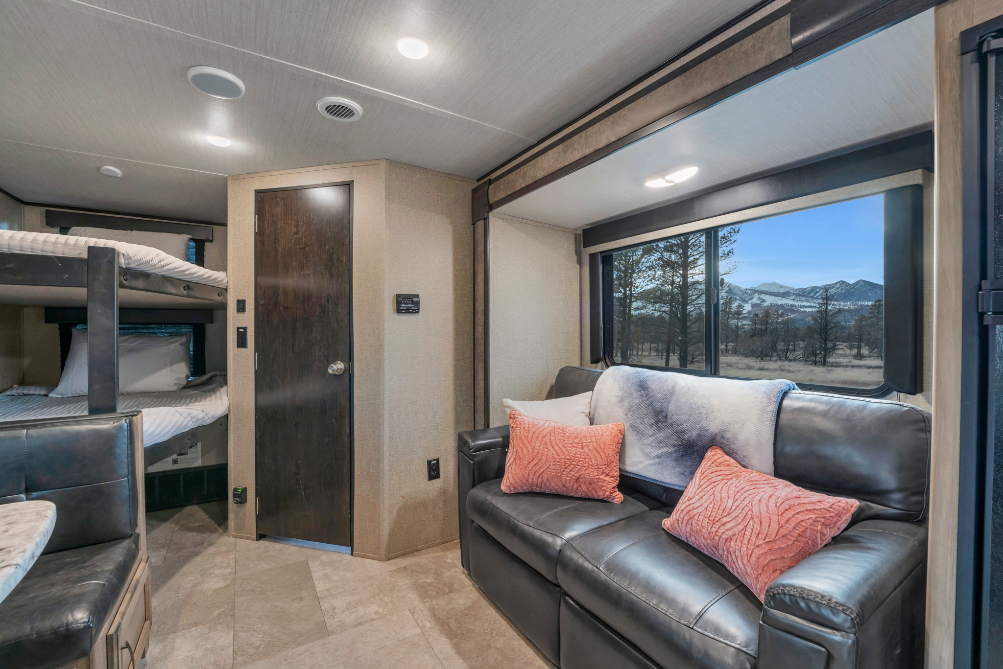 Modern RV rental interior with a plush sofa, bunk beds, and a stunning snowy mountain landscape visible through the window.. Grand Design Transcend Xplor 2020