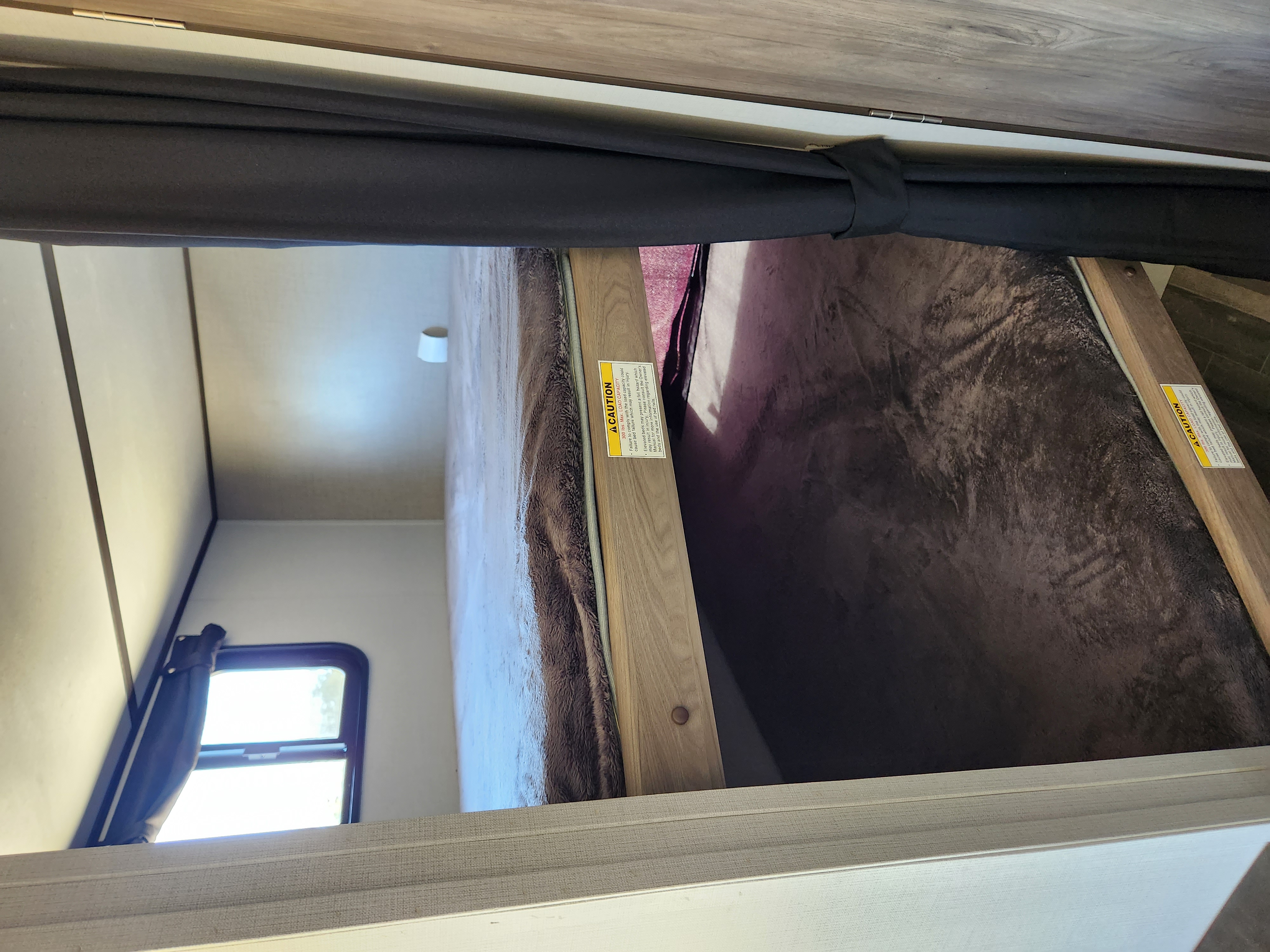Inside an RV rental: cozy bunk beds with a curtain, window, and caution label for load capacity.. Crossroads RV Zinger Lite 2020
