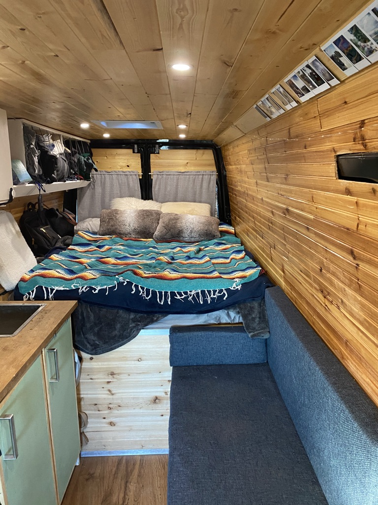 Step inside this inviting RV rental: a wood-paneled camper interior with a cozy bed, sofa, and small kitchen.. Dodge Sprinter 2005