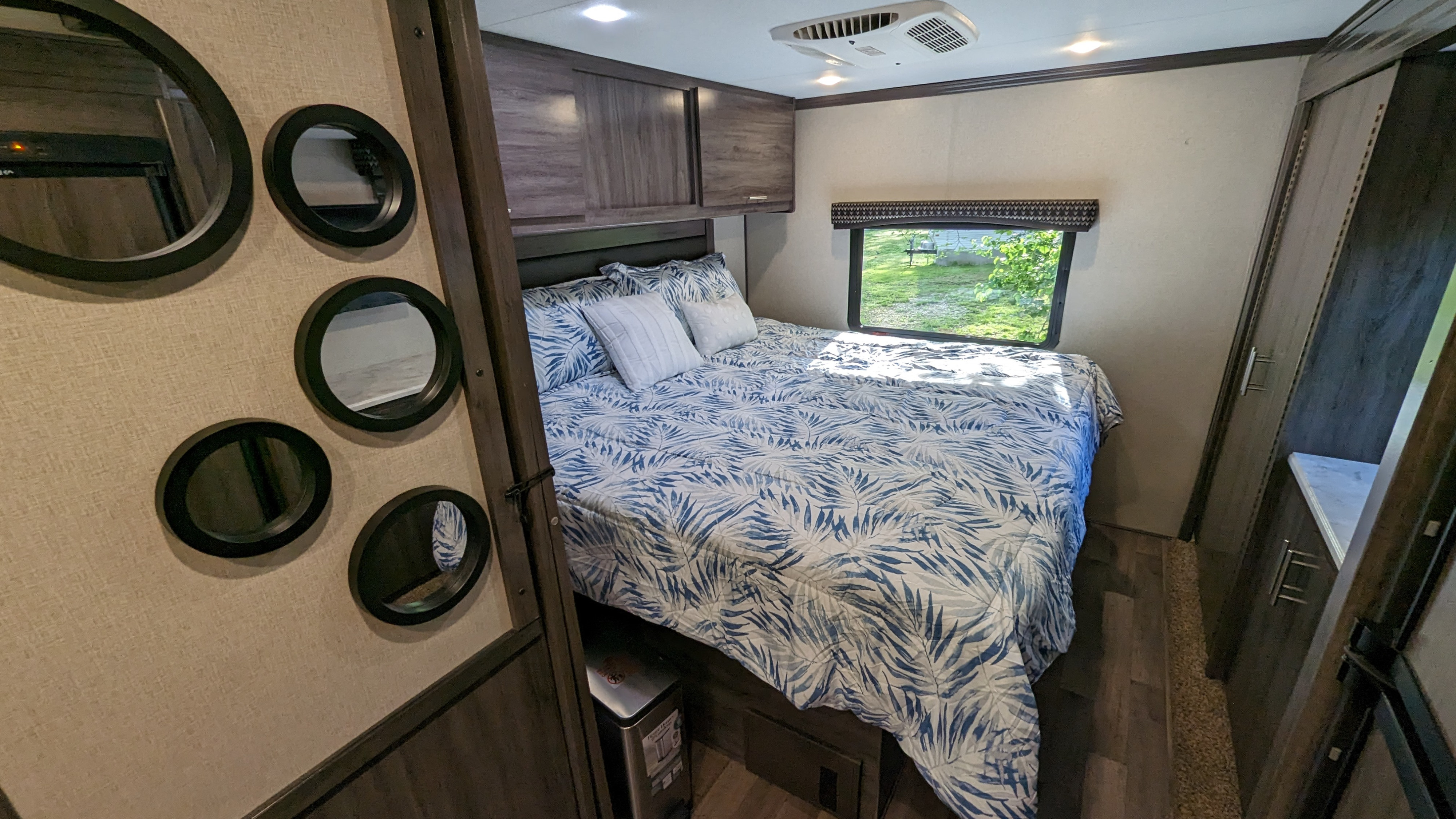Cozy RV rental bedroom showing a comfortable bed, stylish wall mirrors, overhead storage, and a scenic window view.. Fleetwood Axon 2018