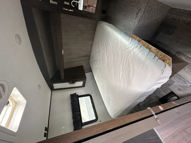 Modern RV rental bedroom interior with clean, wrapped mattress, dark wood cabinets & floor. Ready for travel.. Keystone RV Springdale 2021