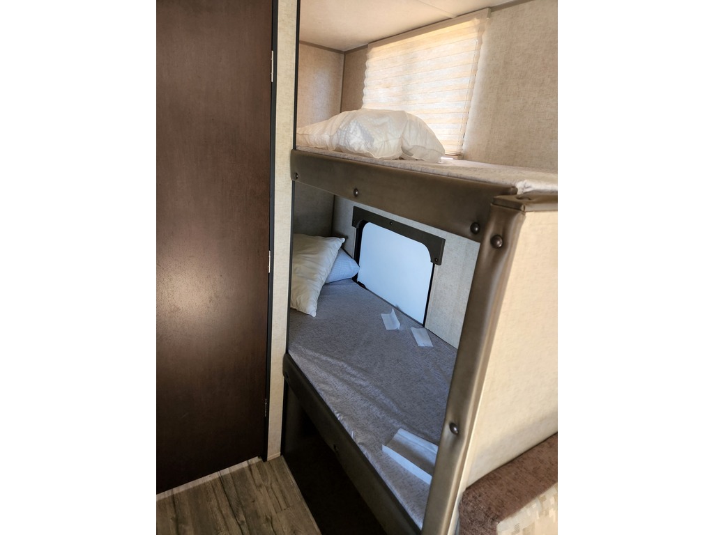 RV rental interior with cozy bunk beds, ideal for family travel. Features include a window with blinds and a small lower bunk opening.. Forest River Cherokee Wolf Pup Cascade 2017