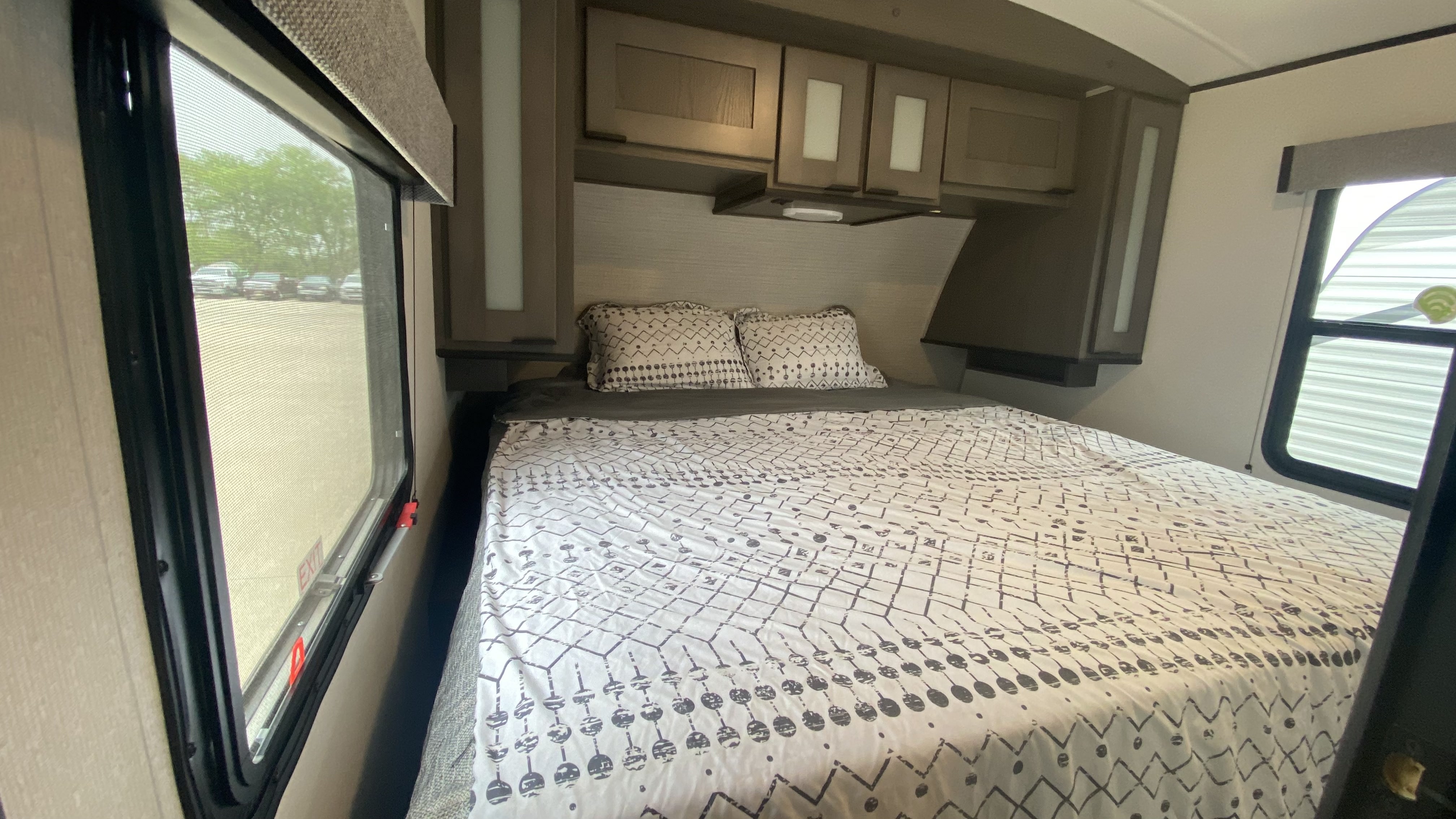 Inside an RV rental, a cozy bedroom with patterned bedding, overhead storage, and large windows offers comfort.. Cruiser Rv Corp Cruiser 2021