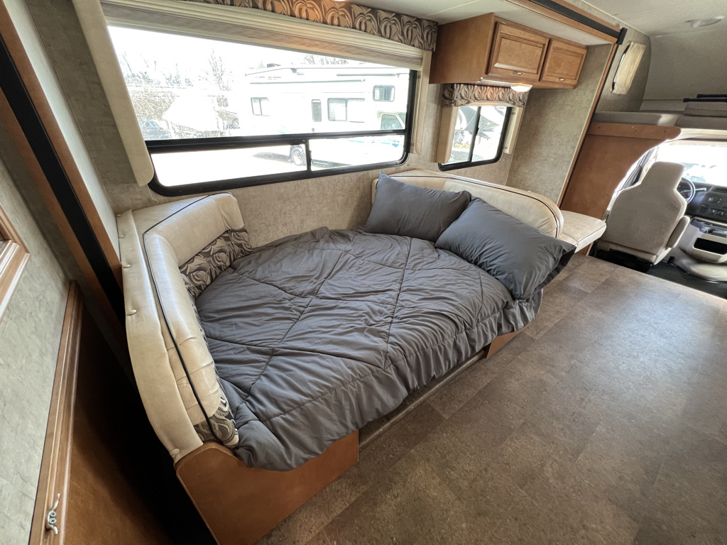 RV rental interior featuring a gray bed/couch, windows, and view of the front driver's cab.. Winnebago Minnie Winnie 2015
