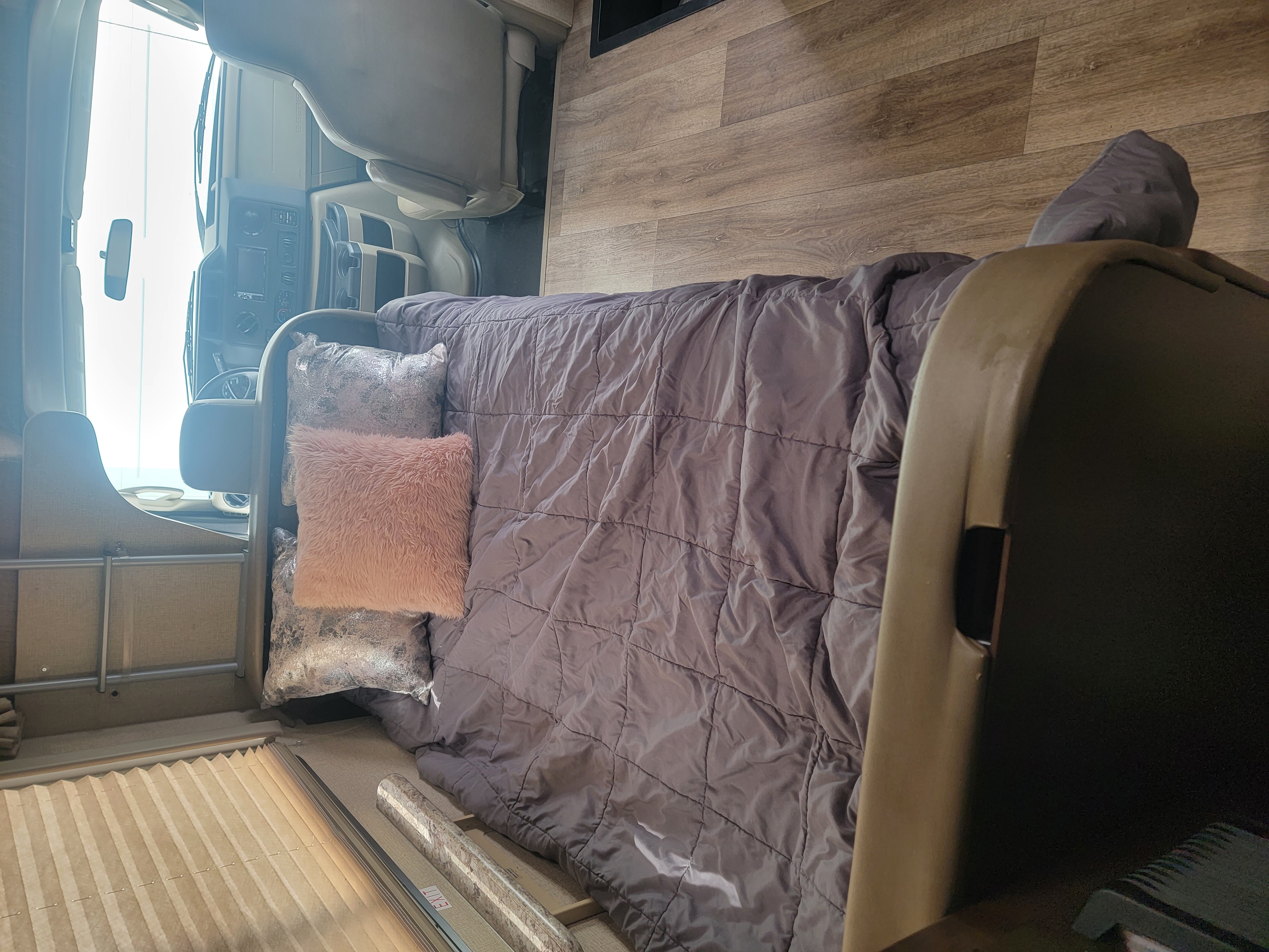 RV rental interior: The driver's cabin is visible in the background, with a cozy bed, gray comforter, and pillows in the foreground.. Thor Four Winds 2020