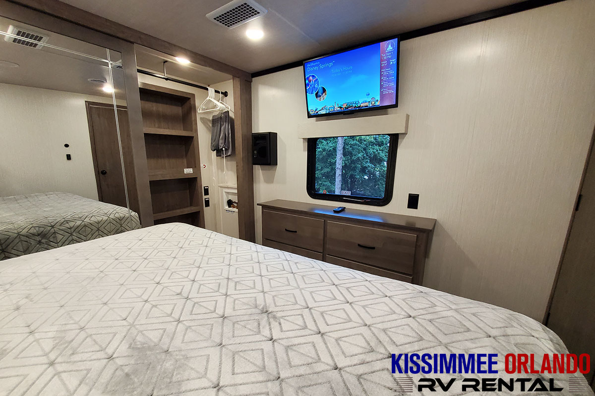Explore this comfortable RV rental bedroom, featuring a large bed, TV, dresser, and built-in storage.. Forest River Cedar Creek Fifth Wheel 2022