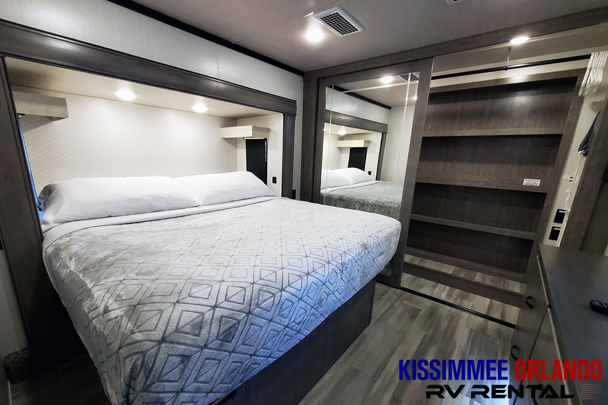 Explore this inviting RV bedroom featuring a comfortable bed, integrated lighting, and ample mirrored storage. Your RV rental awaits!. Forest River Cedar Creek Fifth Wheel 2022