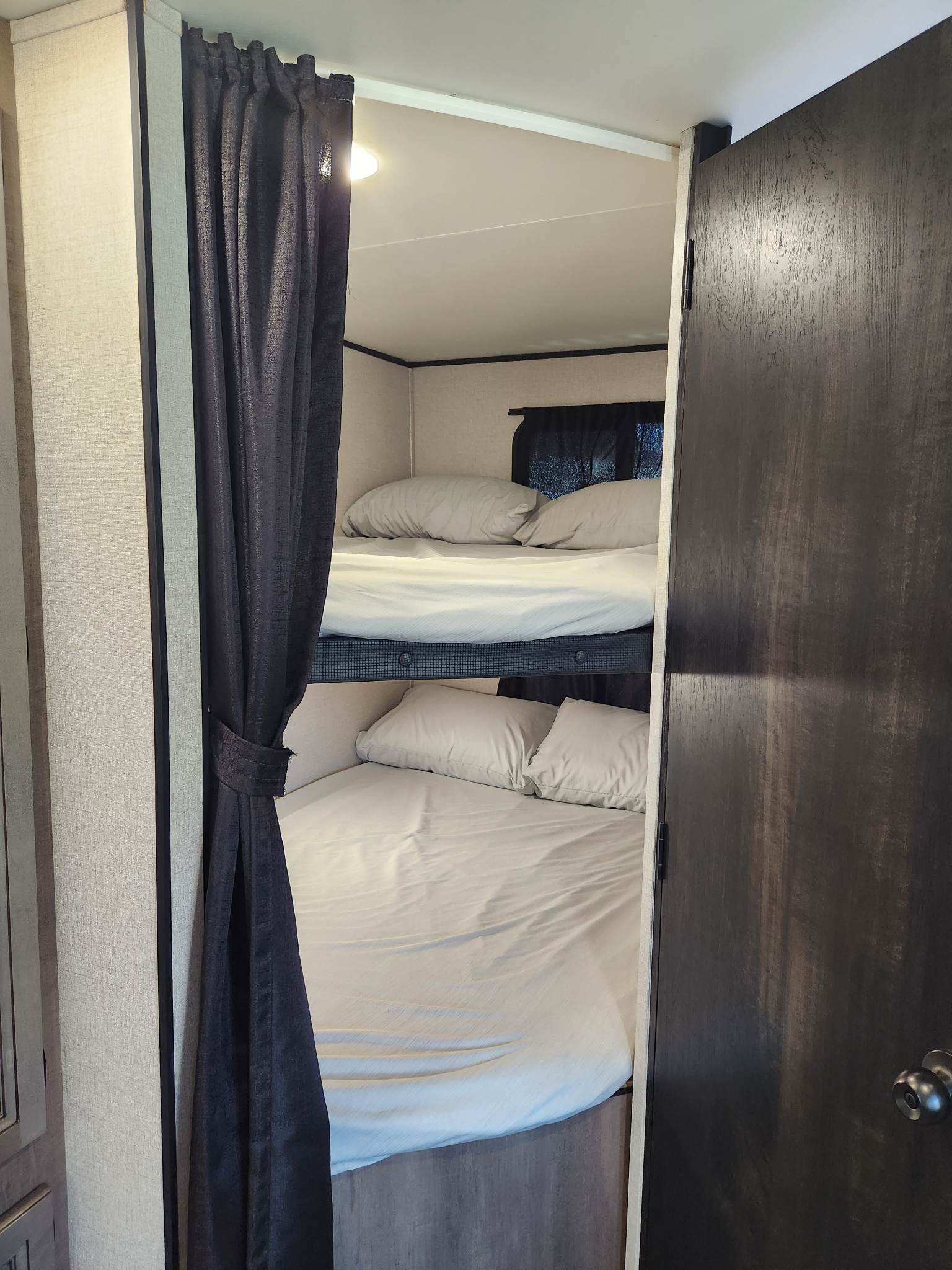 RV rental interior featuring cozy bunk beds with light bedding. A dark curtain is tied back, revealing the sleeping area.. Starcraft Autumn Ridge 2022