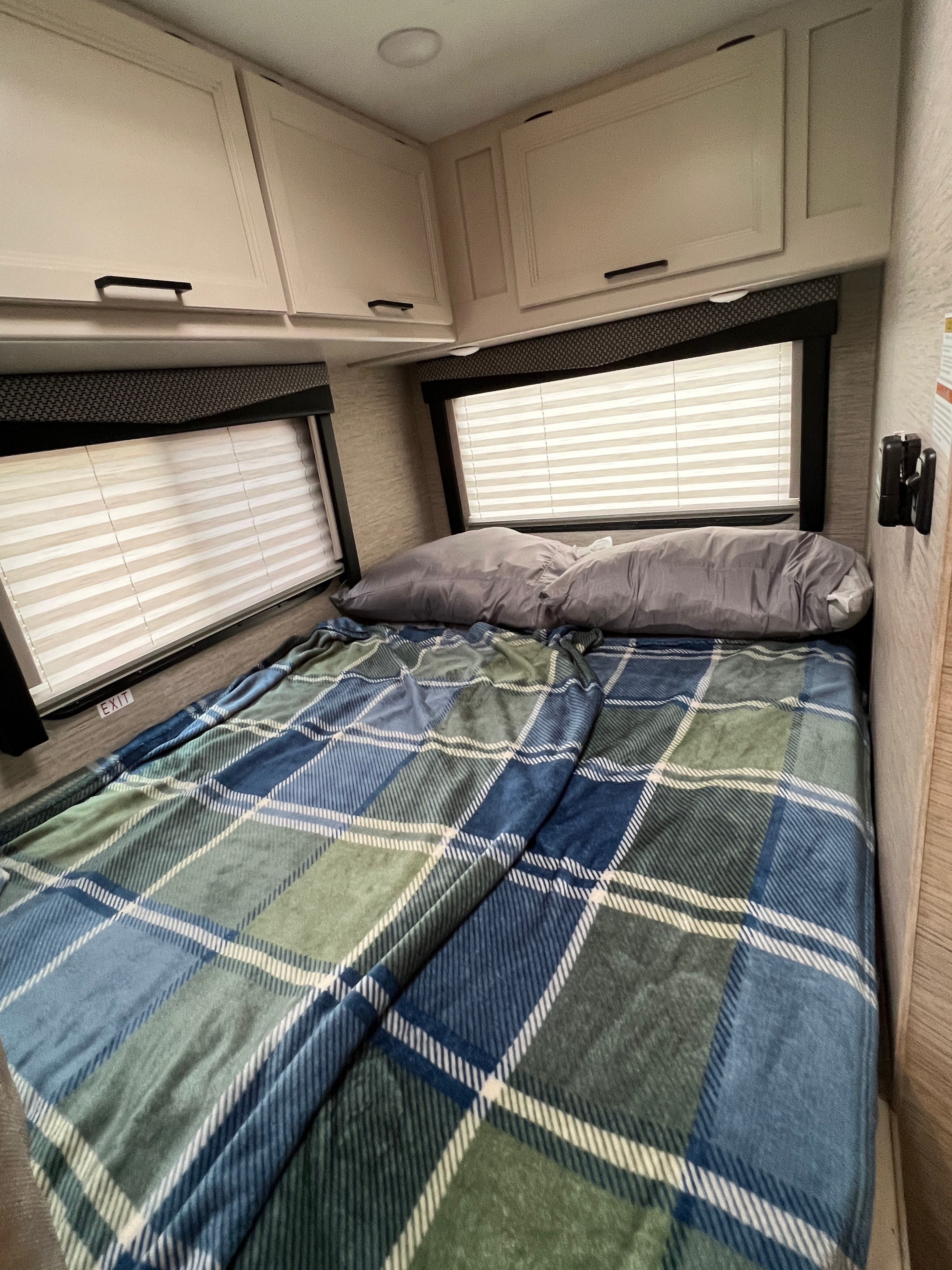 RV rental bedroom: cozy bed with plaid blanket, pillows, windows, and overhead storage.. Thor Freedom Elite 2023